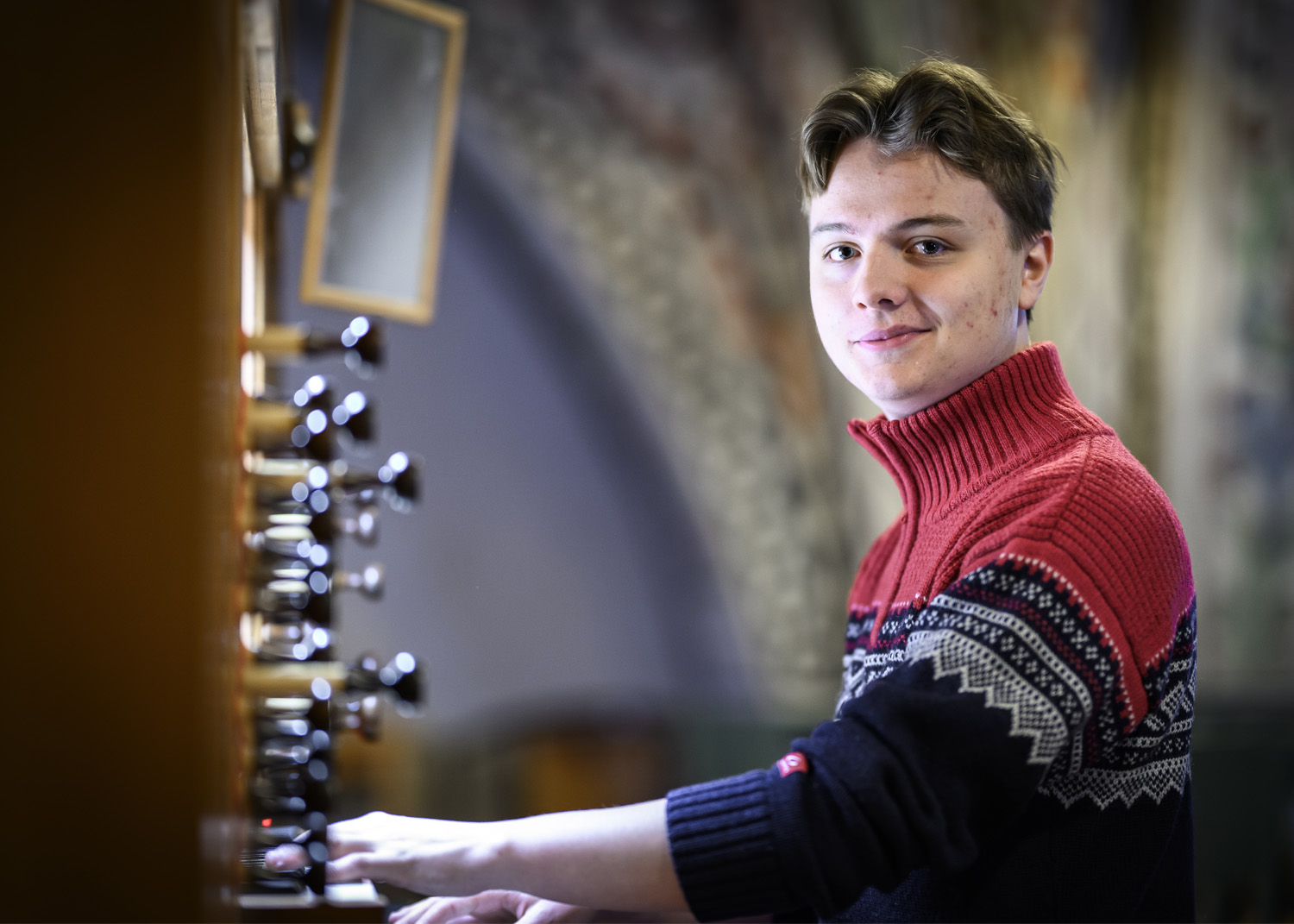 En ung man sitter vid en kyrkorgel. Han tittar in i kameran.