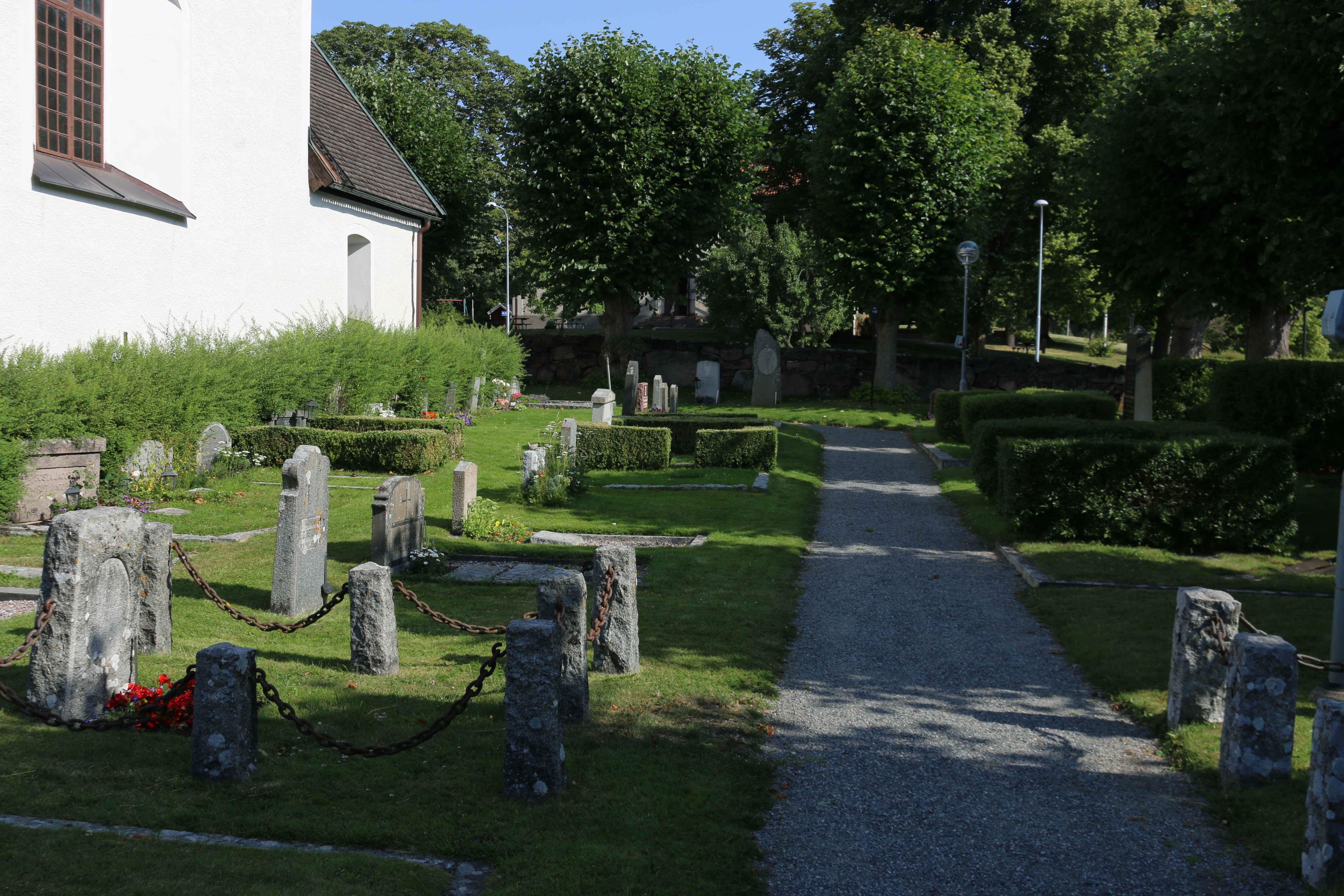 Del av Täby kyrkogård. Utöver gravar och grusgång syns lövverk, träd och en del av kyrkoväggen.