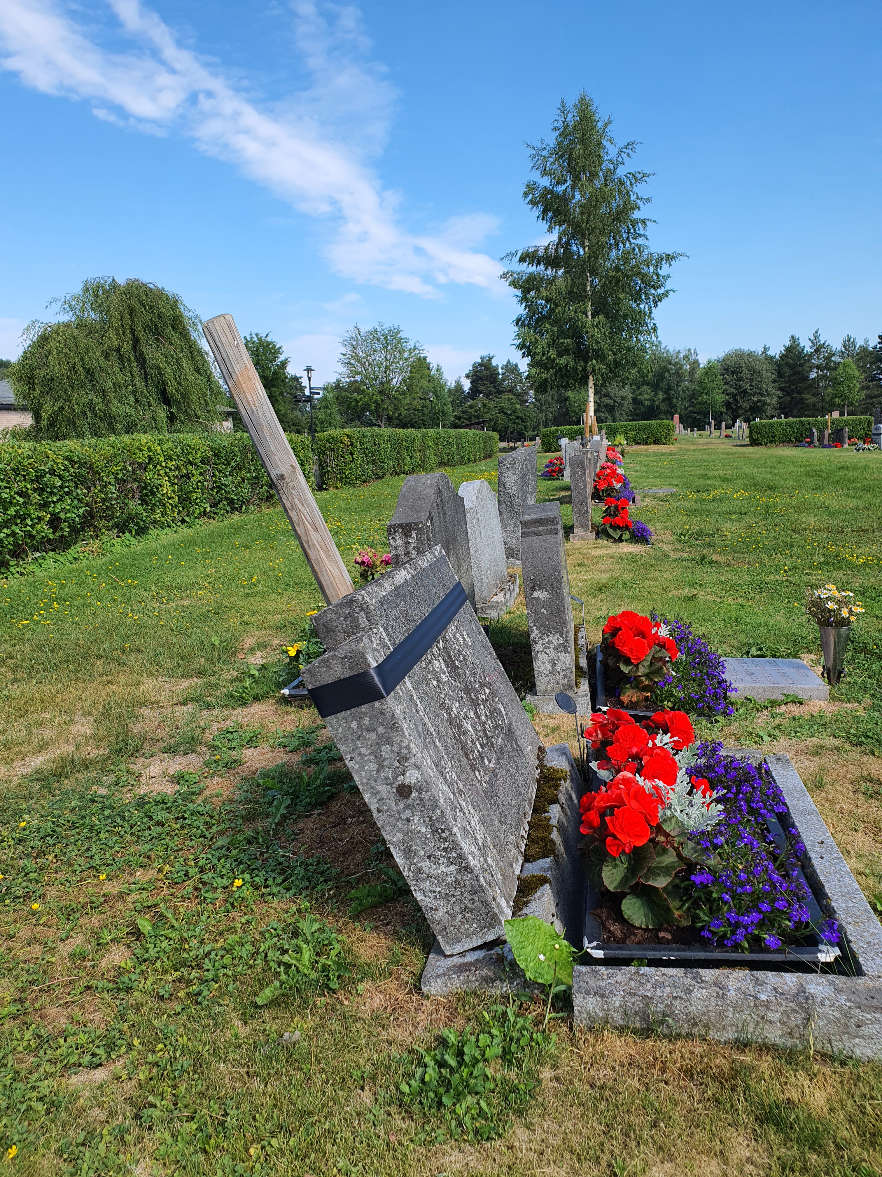 Lutande gravsten fastsurrad vid träpåle