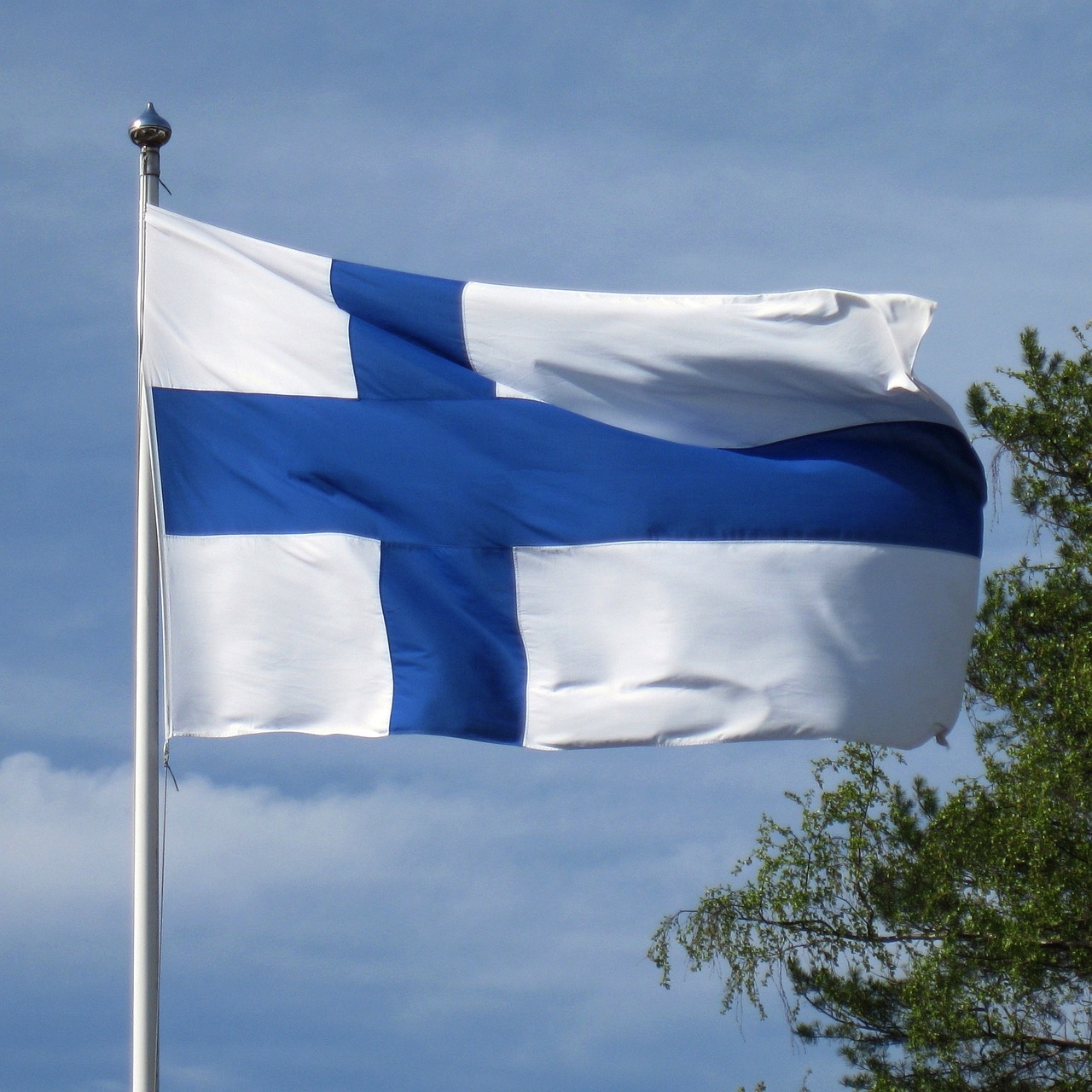 Finsk flagga hissad mot blå himmel.
