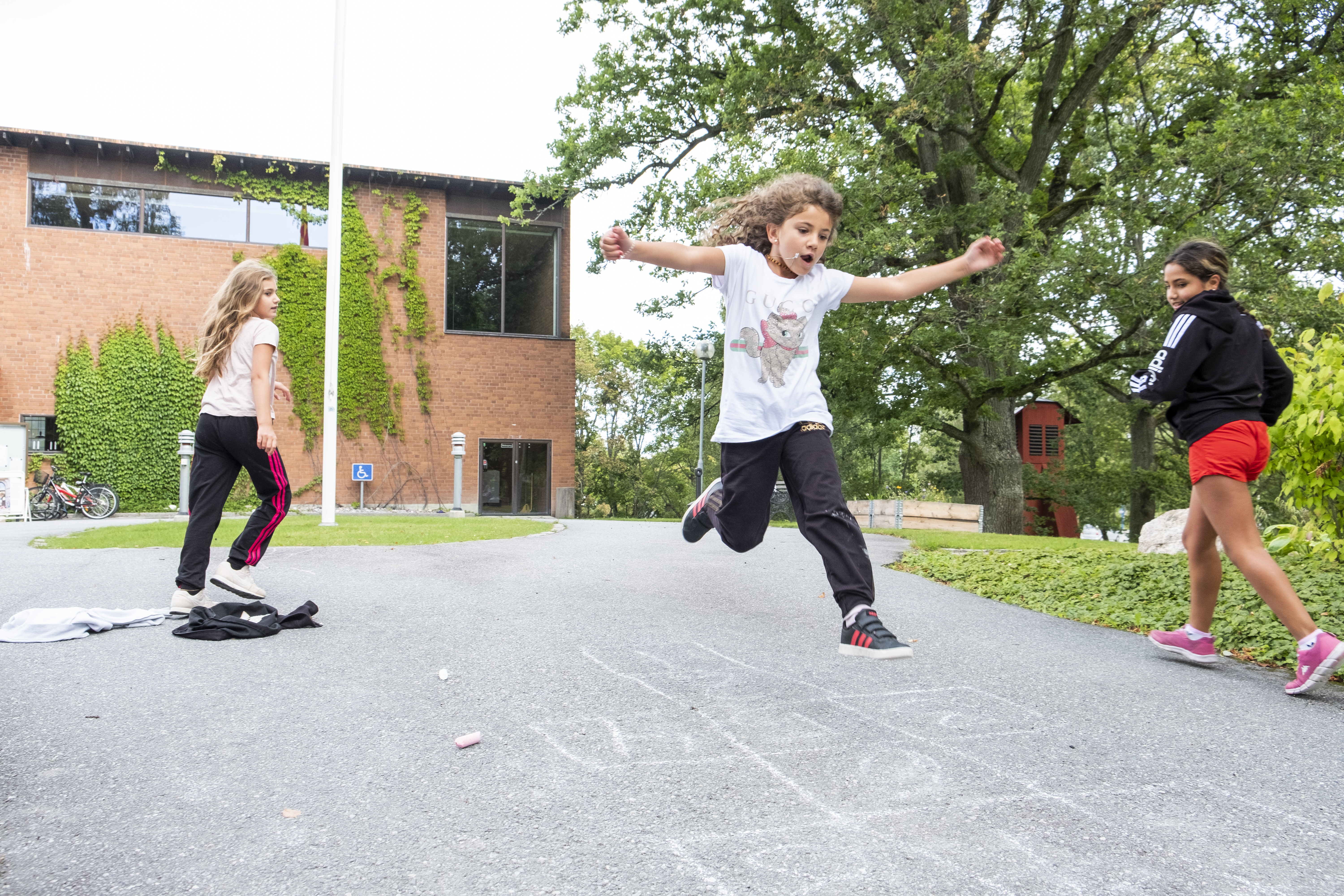 Flicka som hoppar på utritade rutor i asfalten