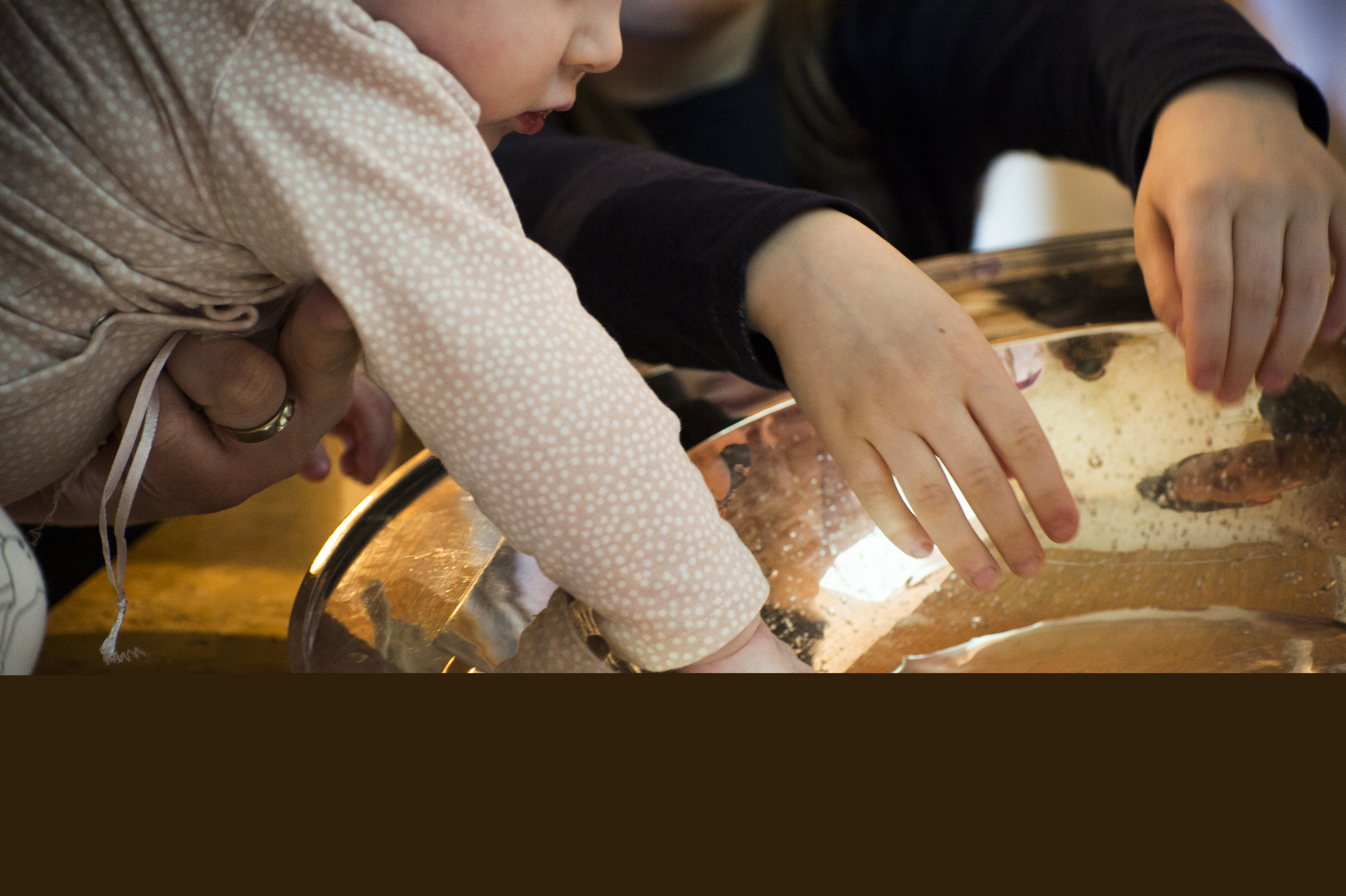 Närbild på dopfunt med barnhänder som rör vid vattnet i dopskålen