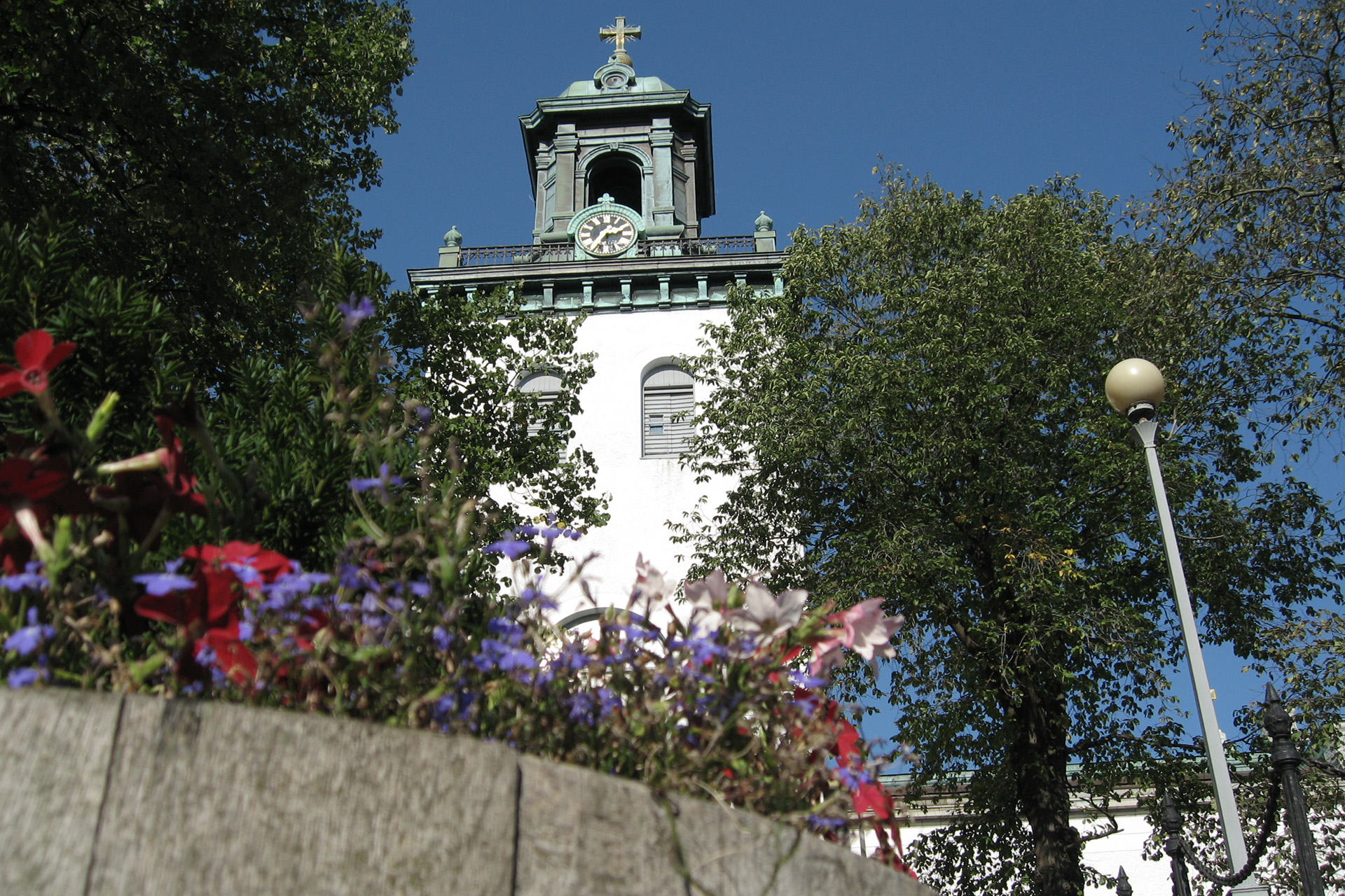 Carl Johans kyrka på sommaren. Framför kyrkan blommar blå och röda blommor.