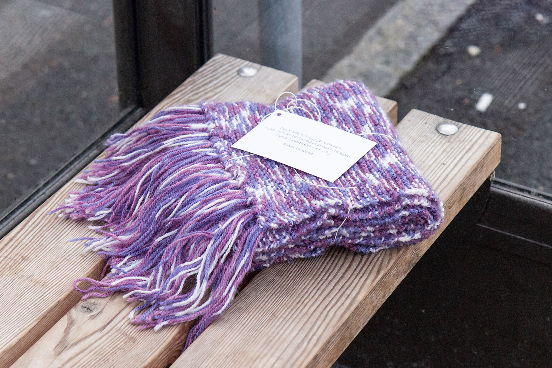 En stickad halsduk placerad på en bänk inuti en busskur.