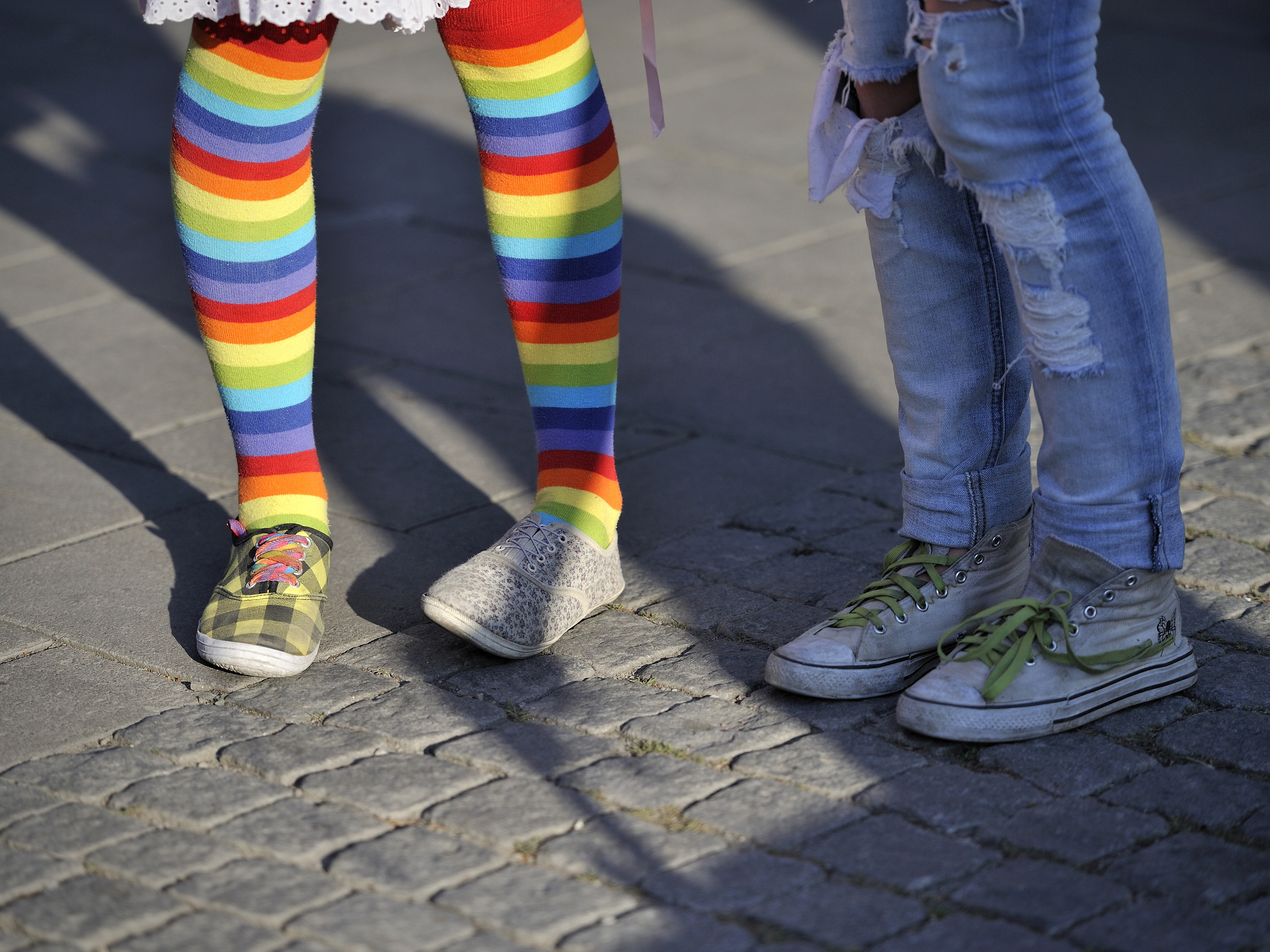 Två barn står bredvid varandra, bara benen syns. Den ena har regnbågsfärgade strumpbyxor.