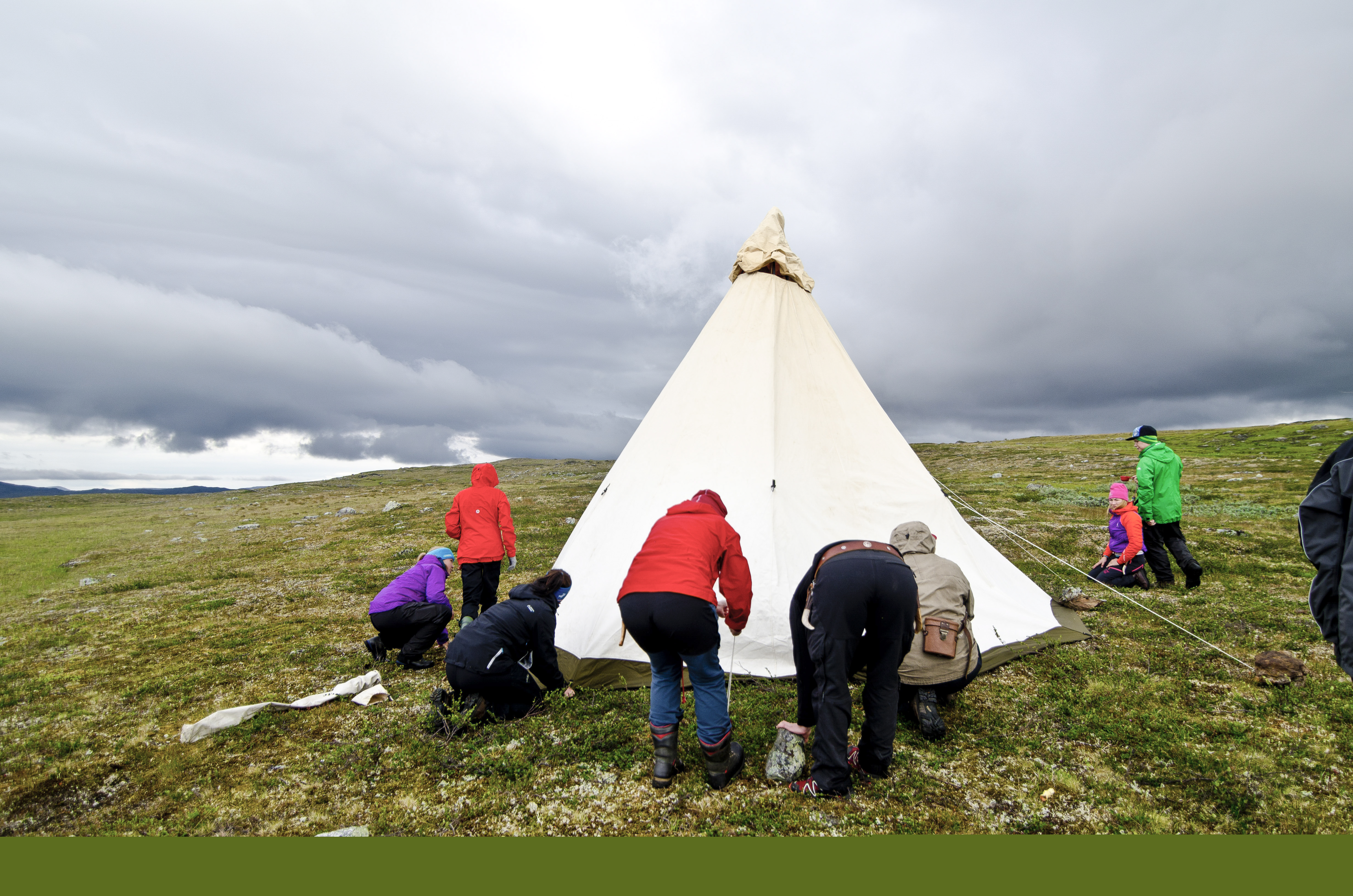 En grupp människor sätter upp ett tält på fjället.