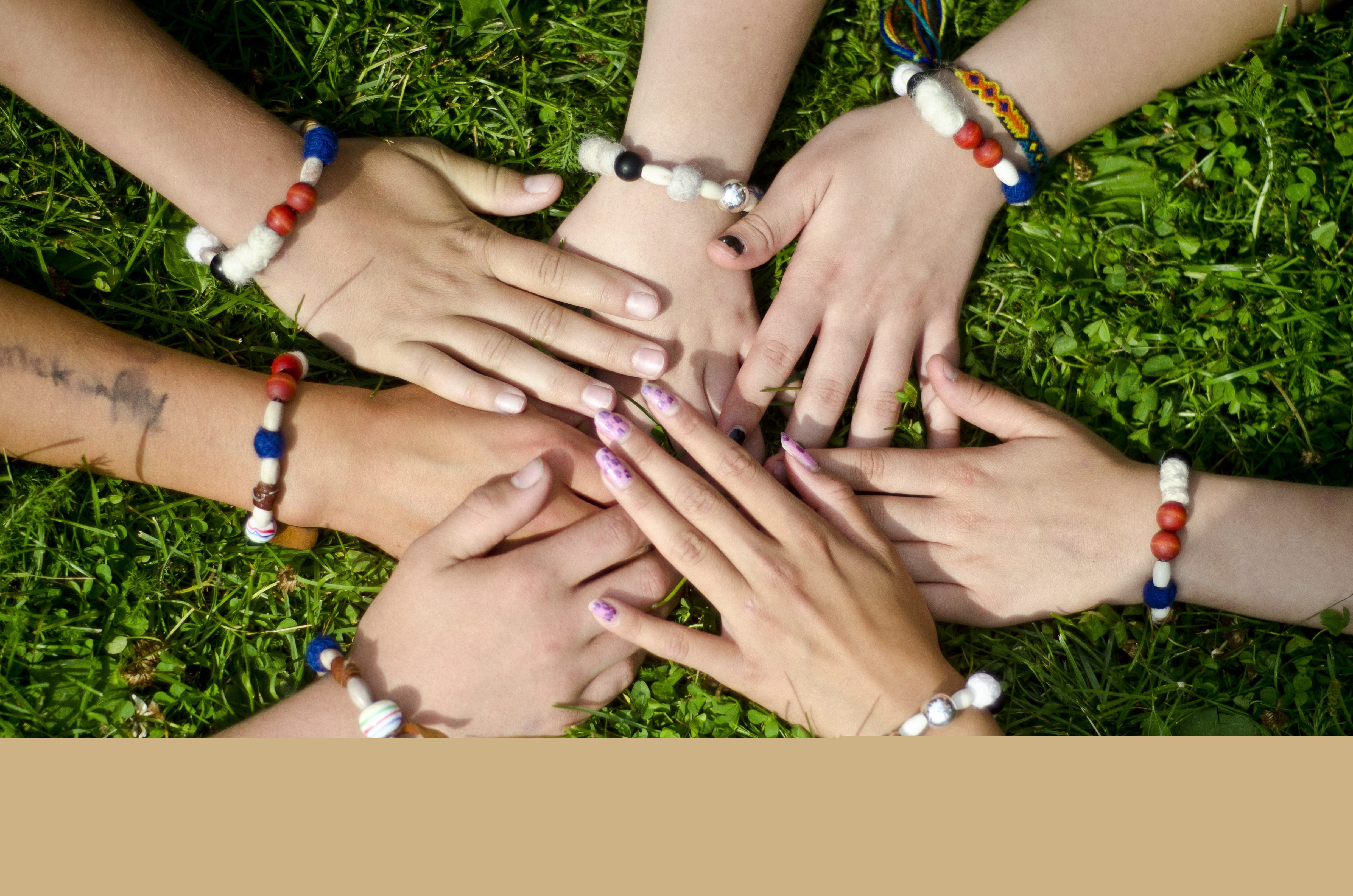 Några personer med varsitt pärlarmband lägger sina händer på varandra i gräset.