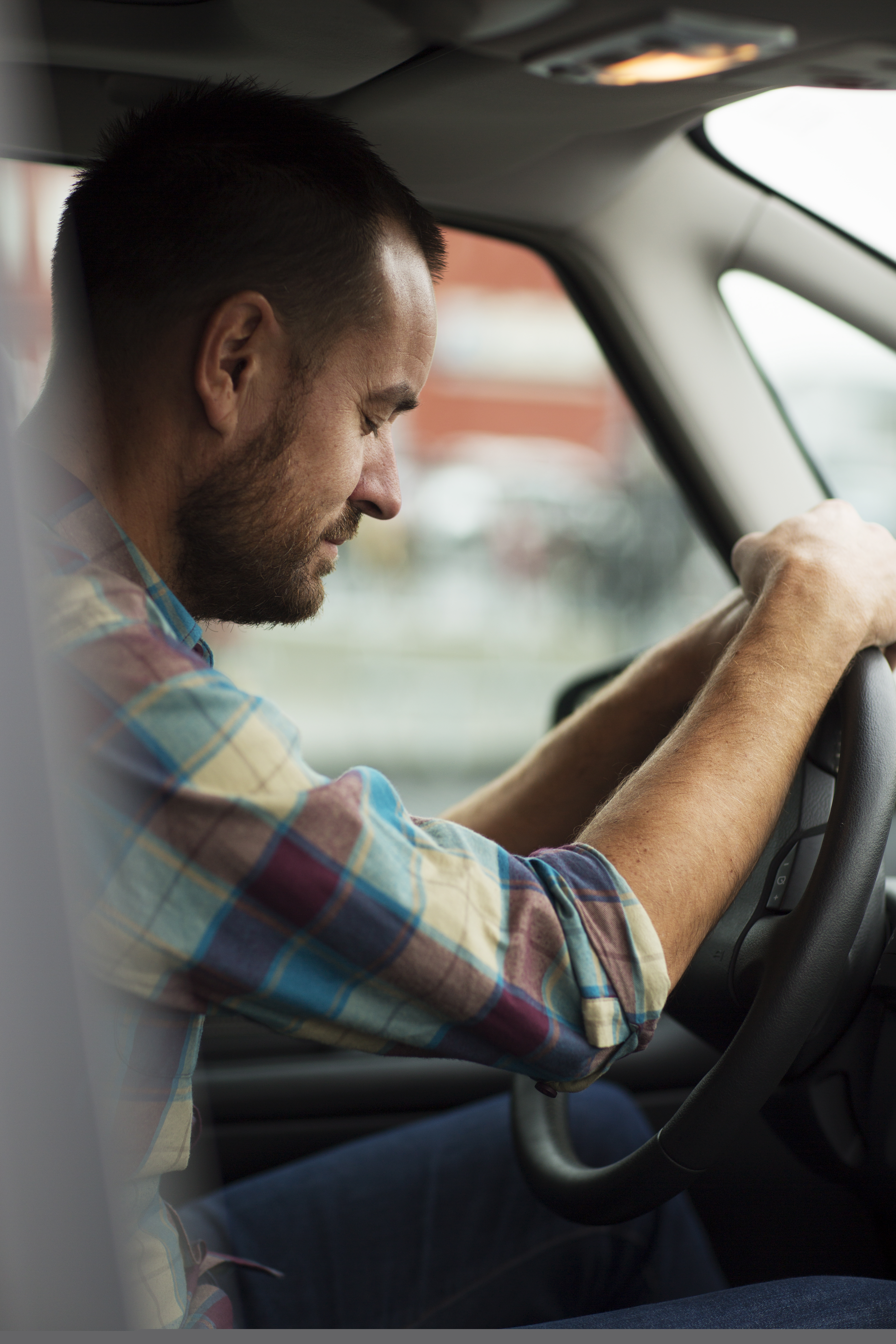 En man sitter i en bil med händerna på ratten och blundar.