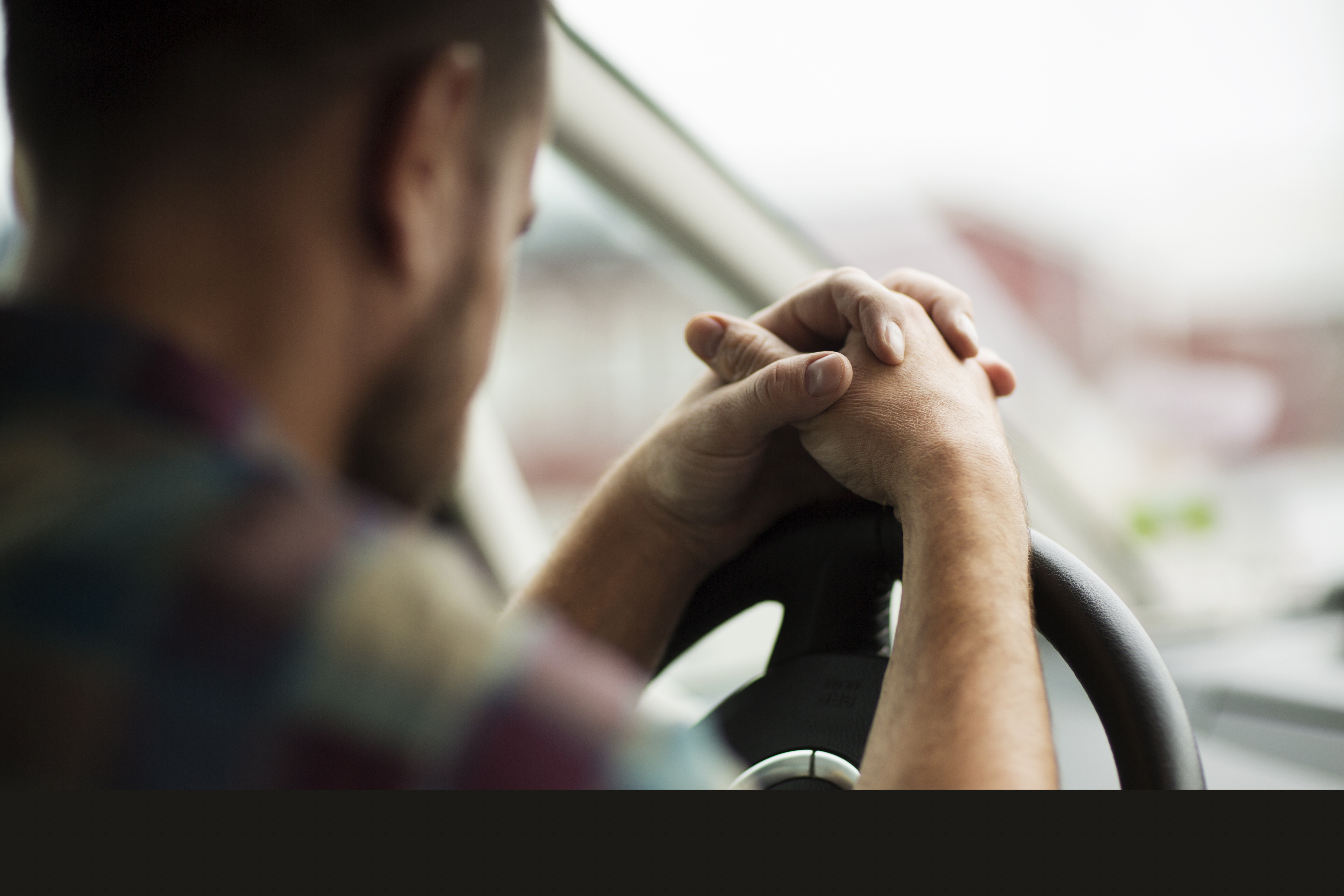 En man sitter i bilen med händerna knäppta på ratten.