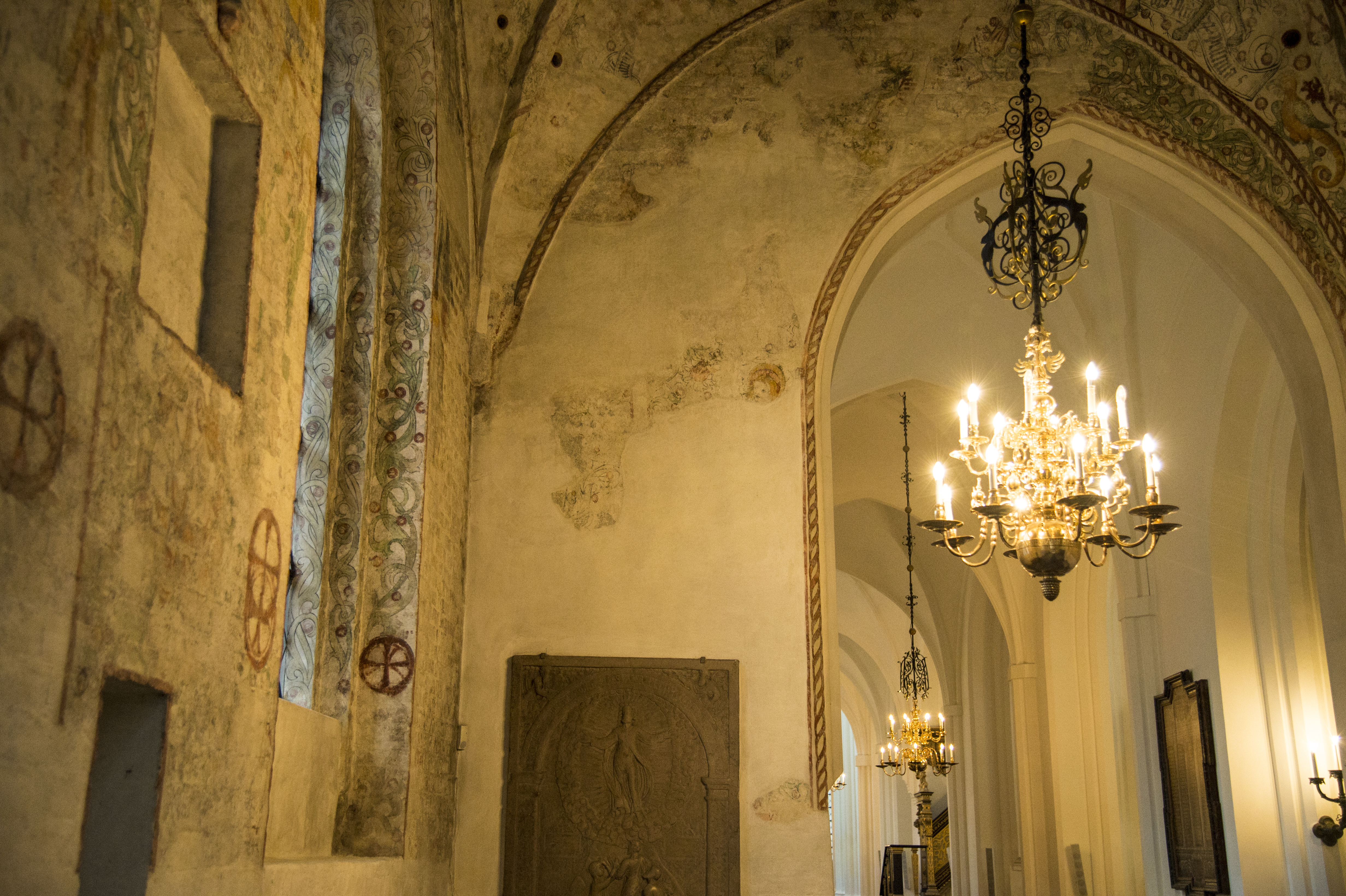 En tänd ljuskrona hänger från taket i en gammal kyrka.