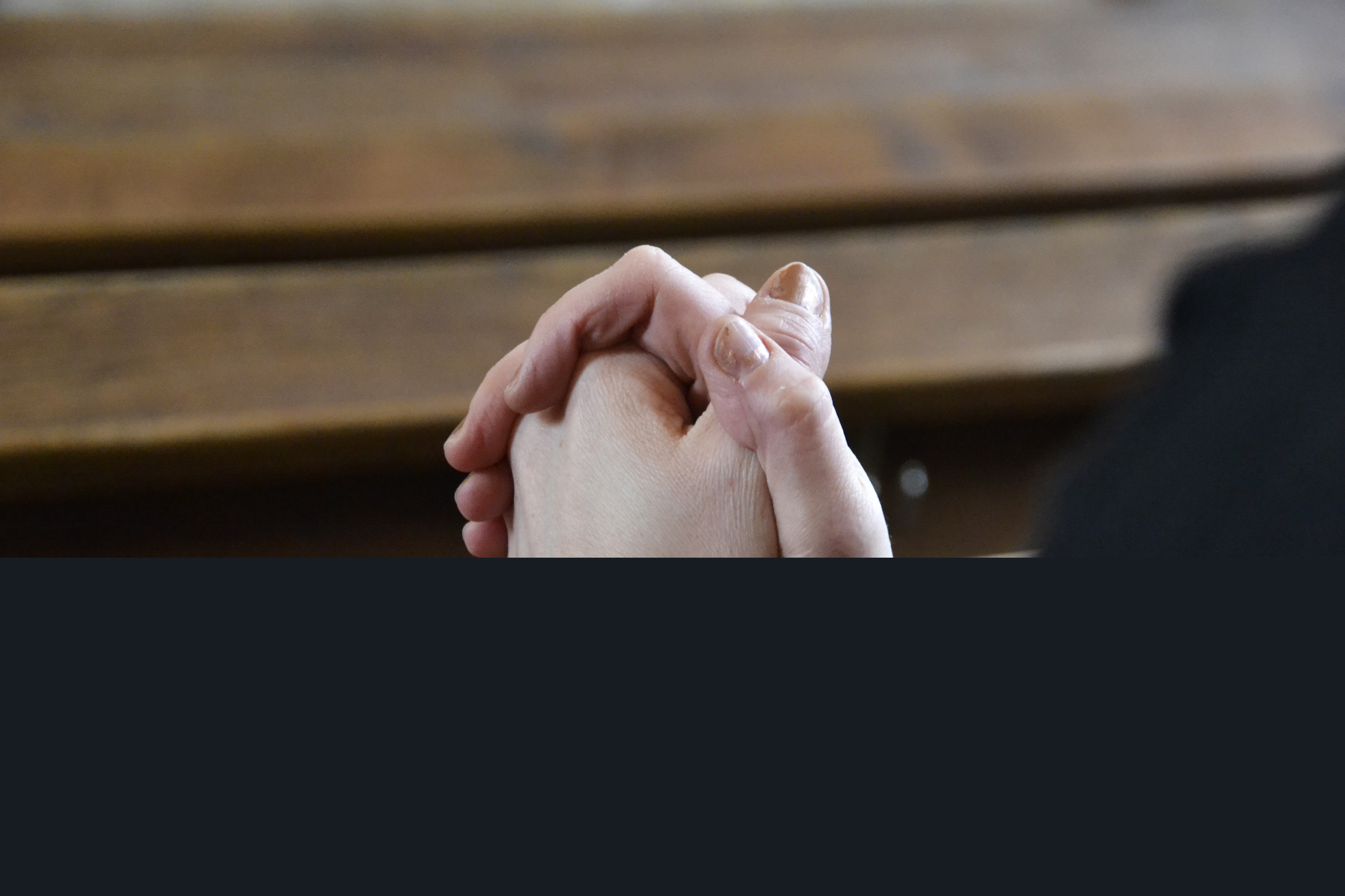 Någon sitter med knäppta händer i kyrkbänken.
