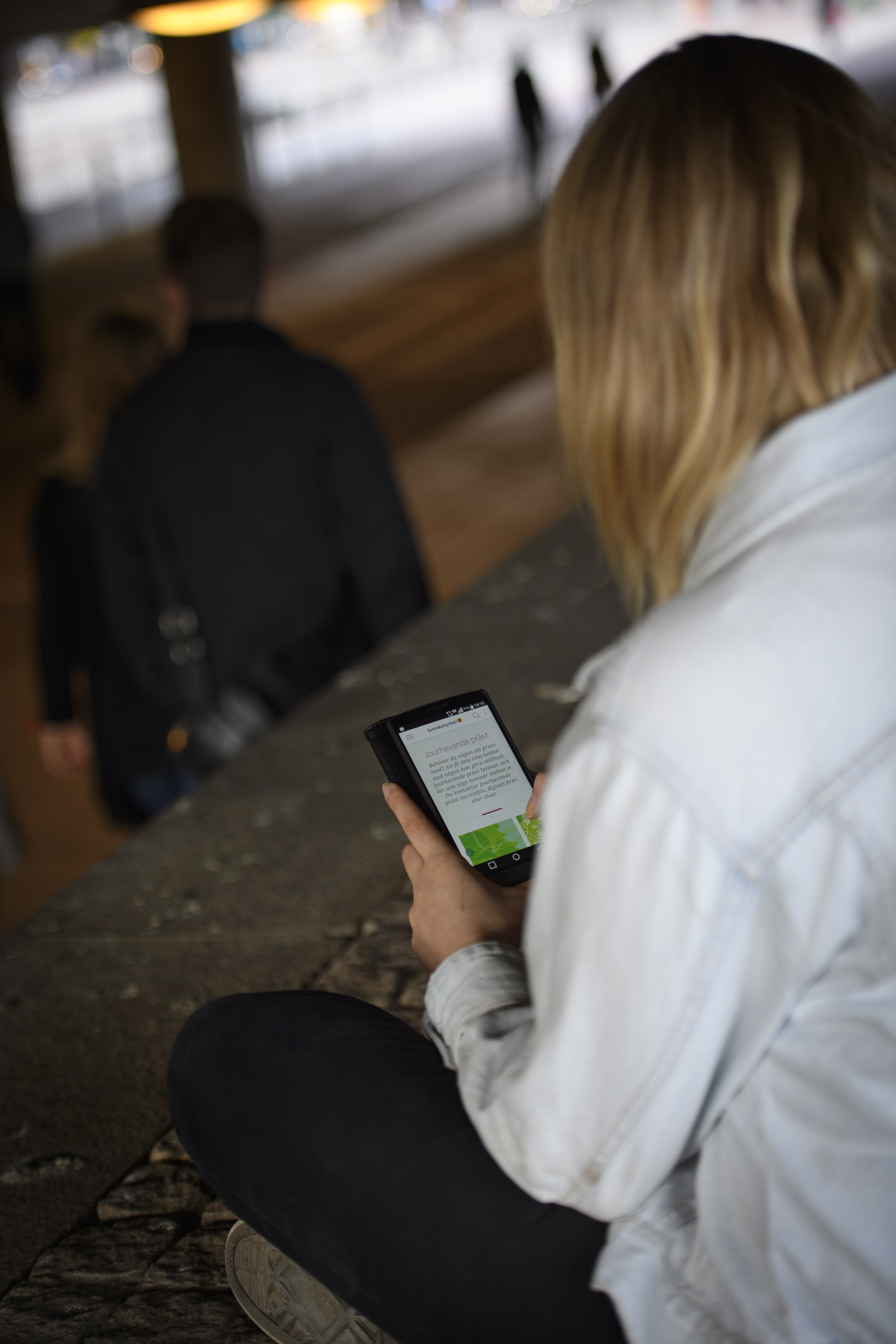 En kvinna sitter utomhus och håller på med sin mobiltelefon.