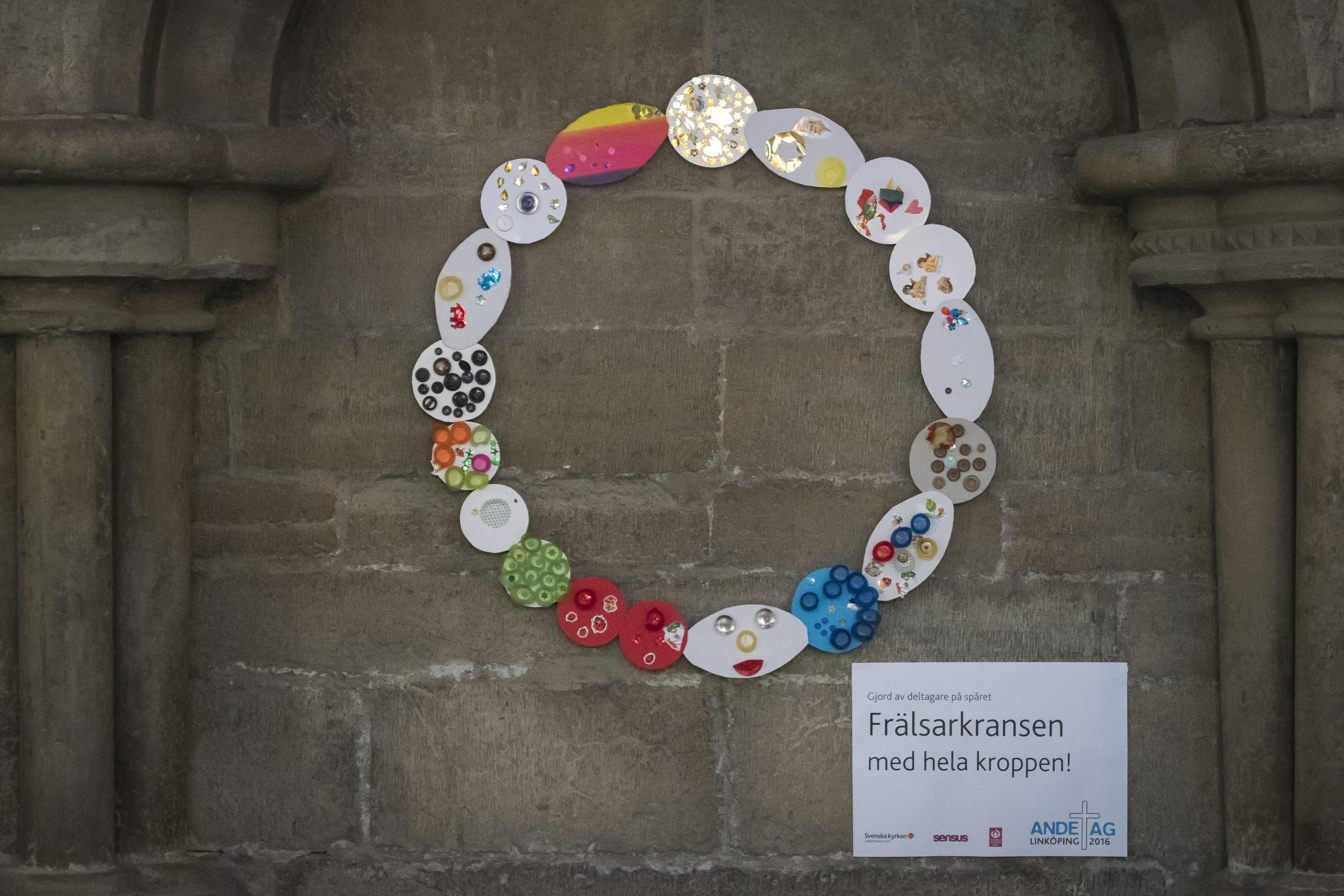 På en vägg i en kyrka hänger en frälsarkrans av papper och olika pärlor.