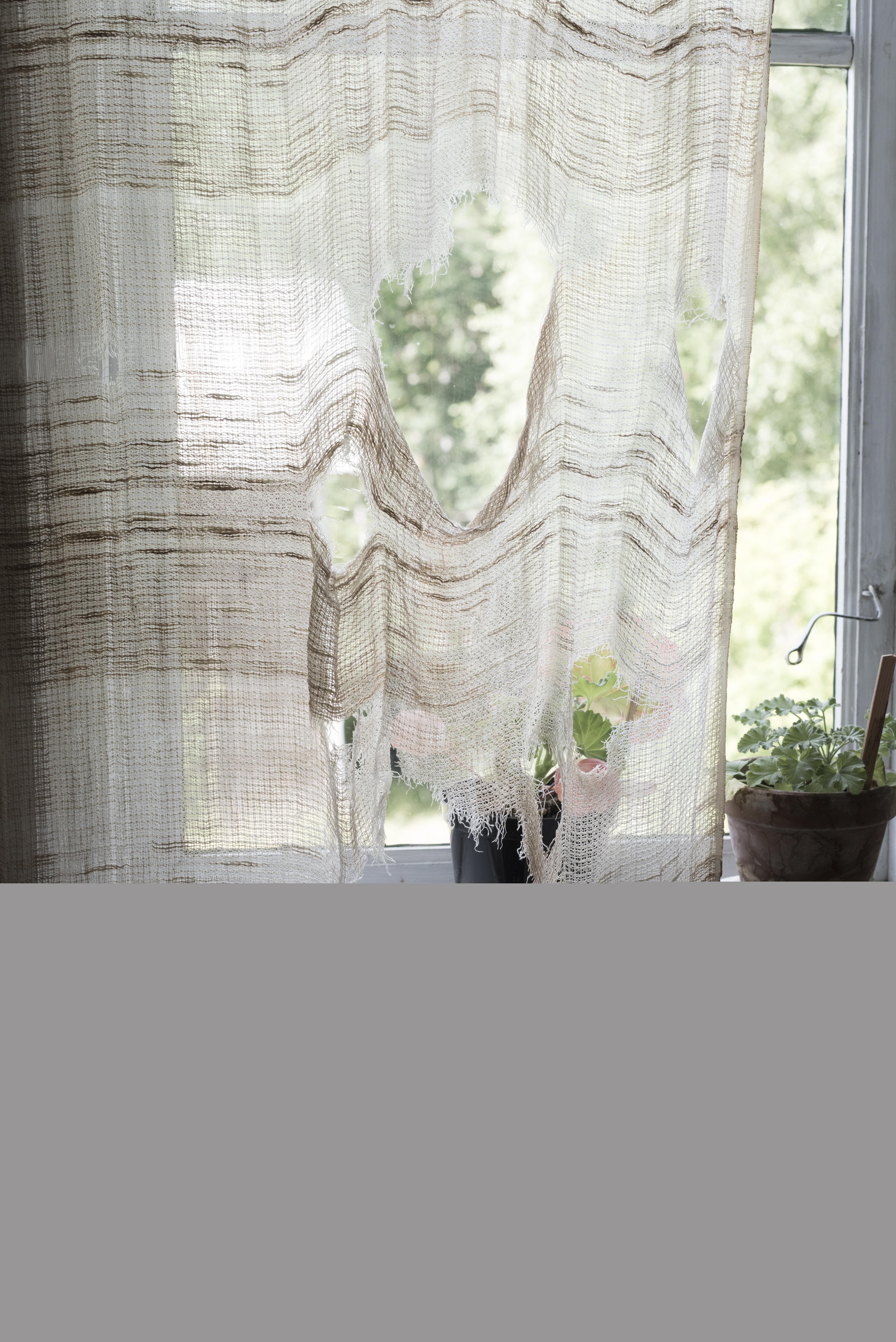 En gammal trasig gardin hänger i ett fönster.