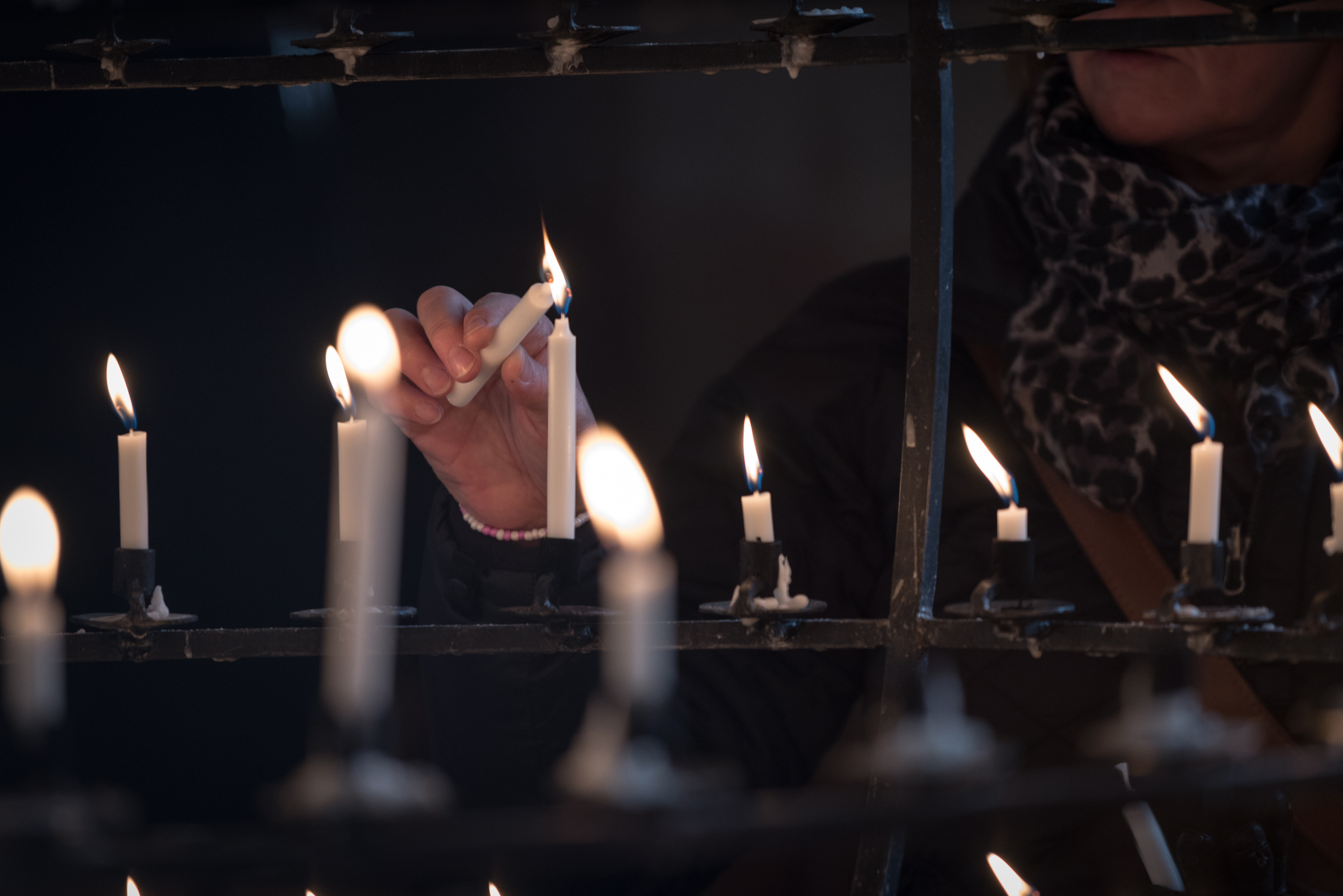 En person tänder ett ljus med hjälp av ett annat ljus i en stor ljusbärare.