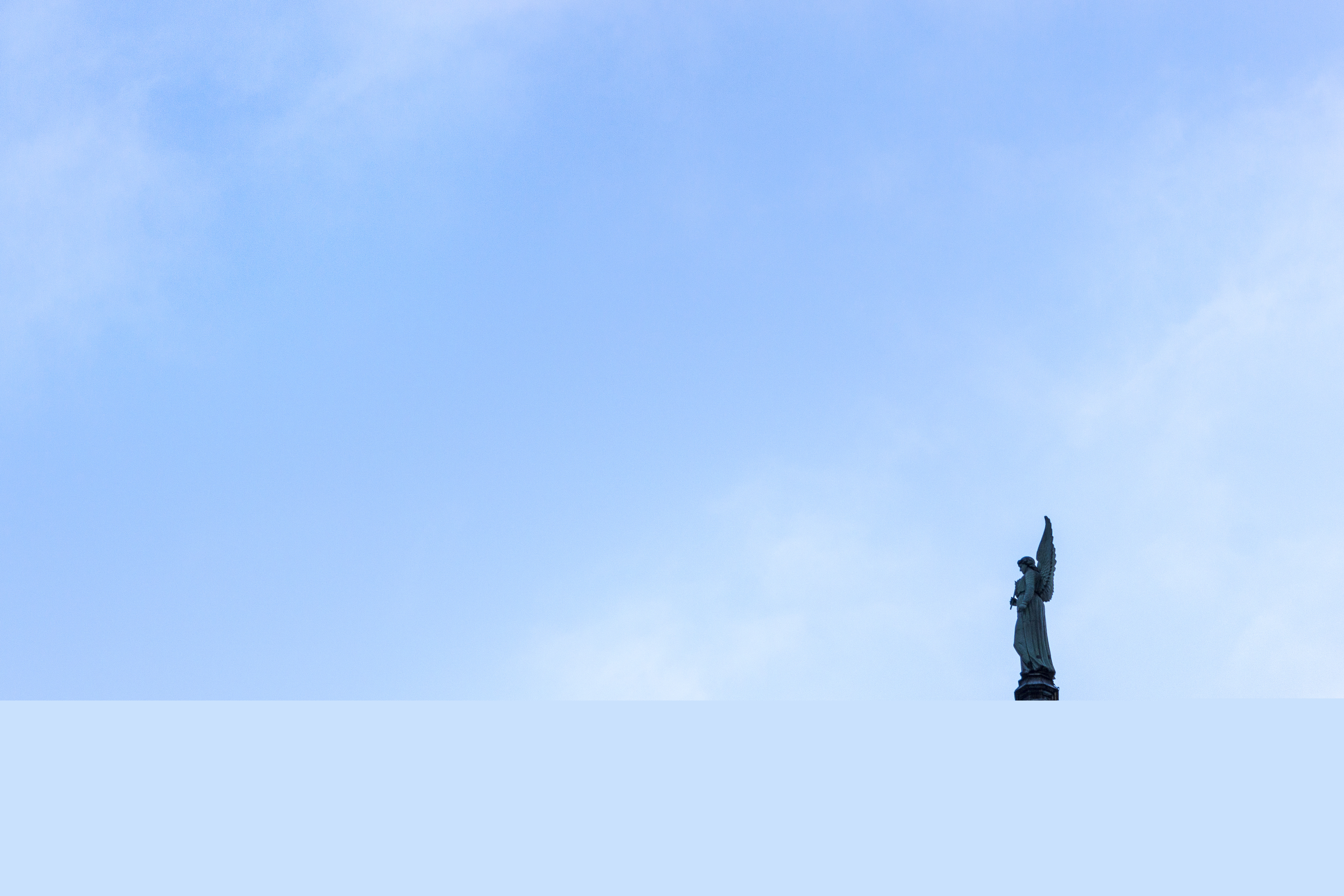 En änglastaty på ett tak mot blå himmel.