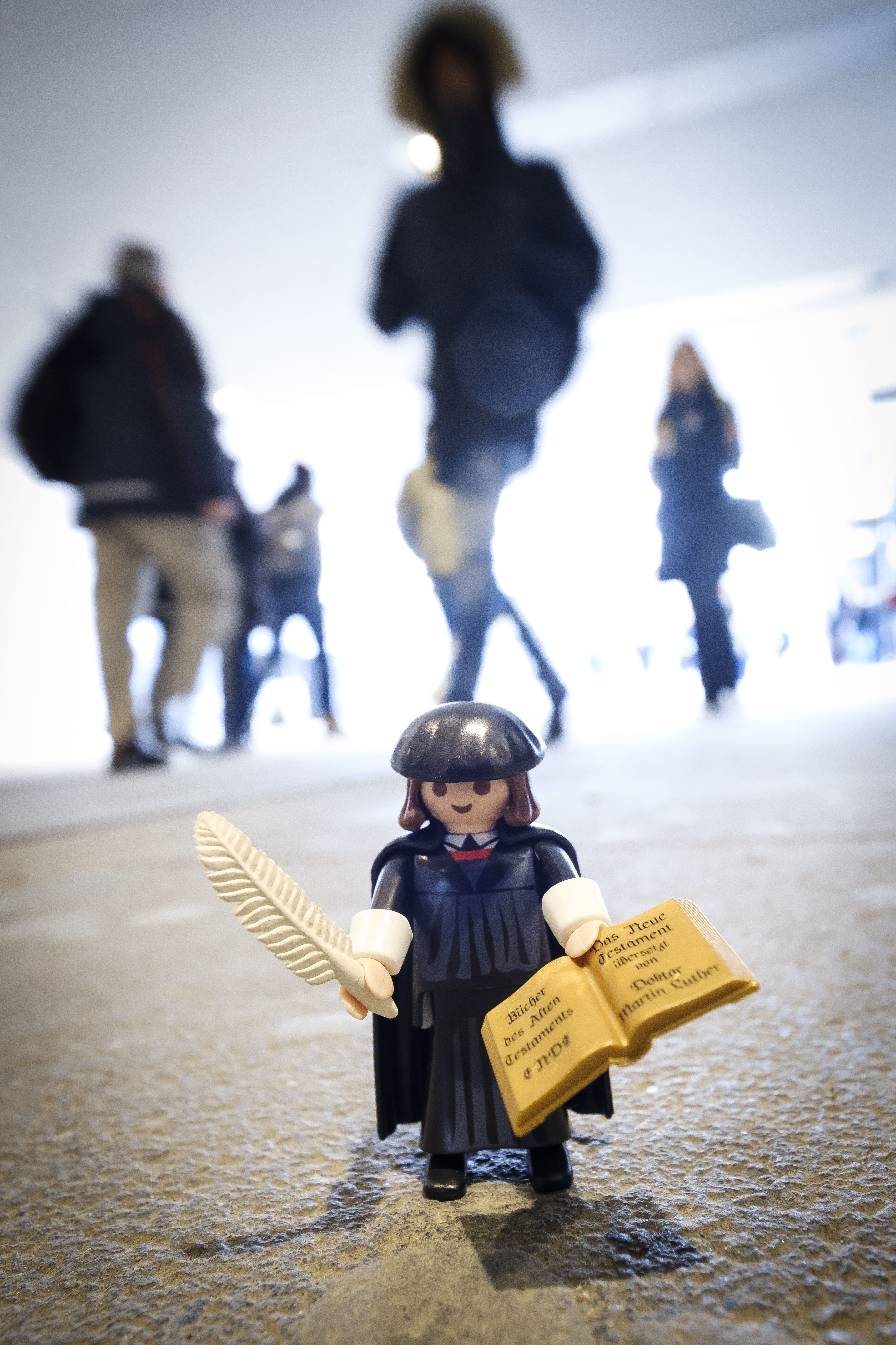 Martin Luther som legofigur står på marken. Människor rör sig runt om.