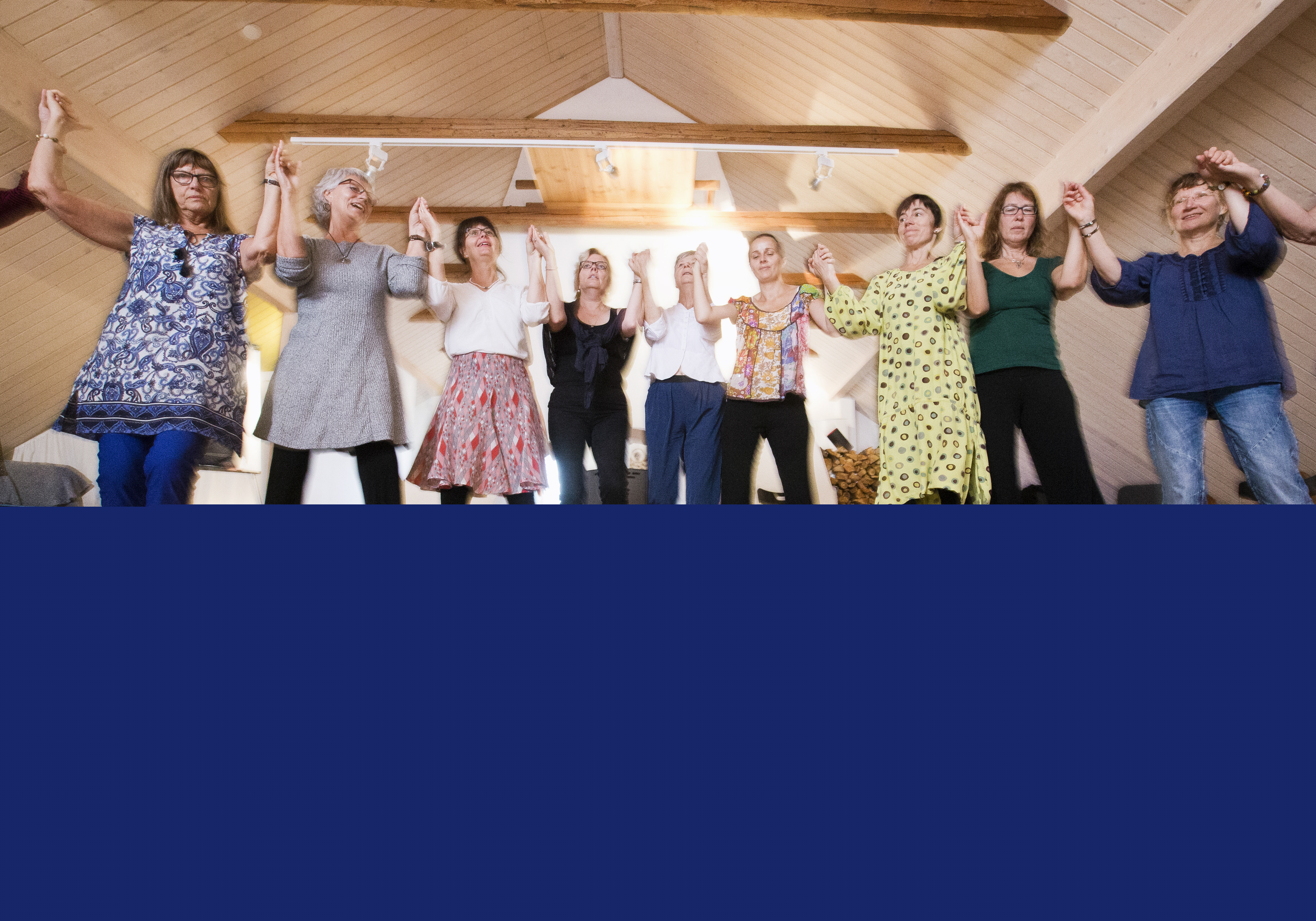 Några kvinnor dansar ringdans runt en skål med vatten och olika frukter som står på golvet.