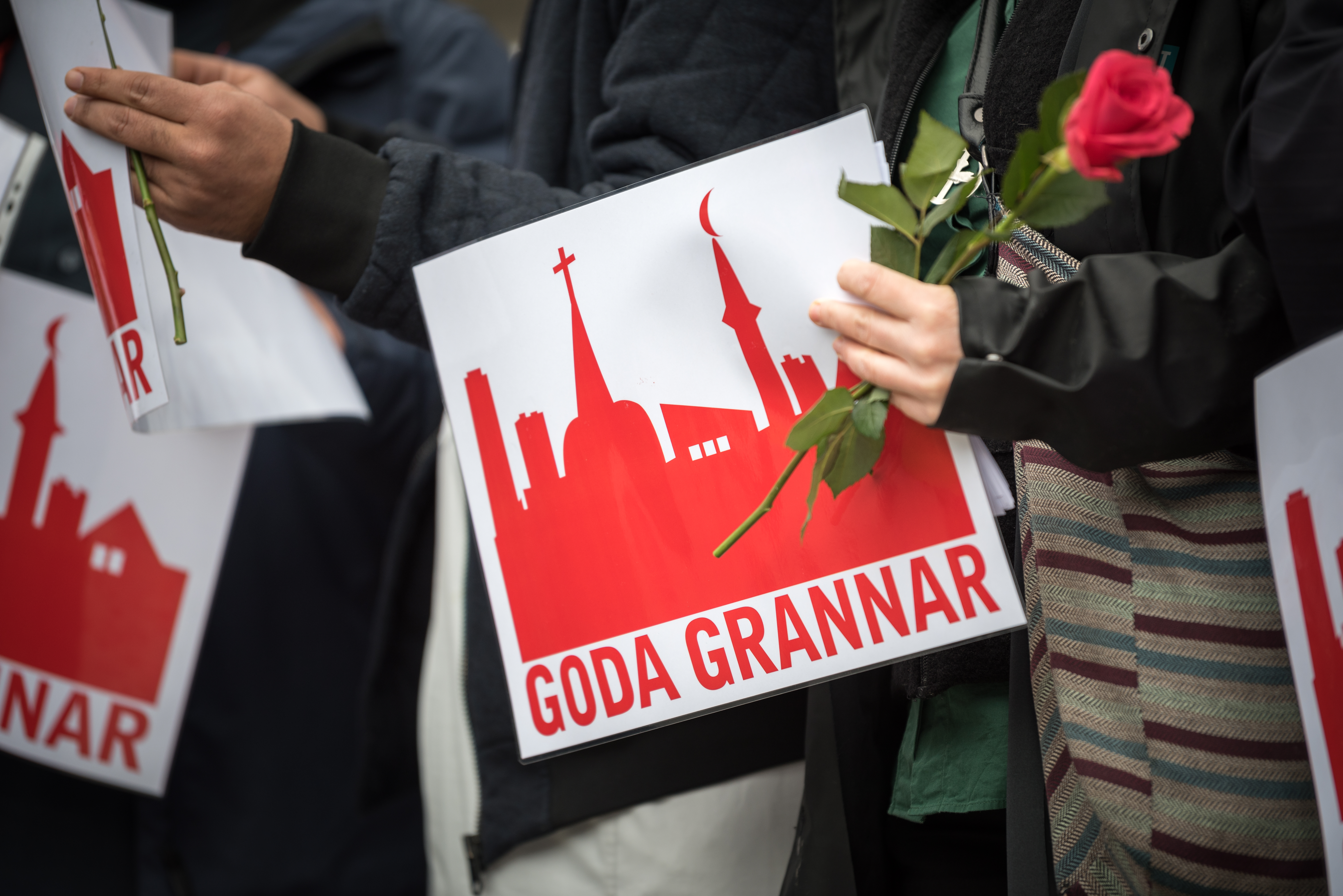 Några människor står med röda rosor och skyltar med texten Goda grannar.
