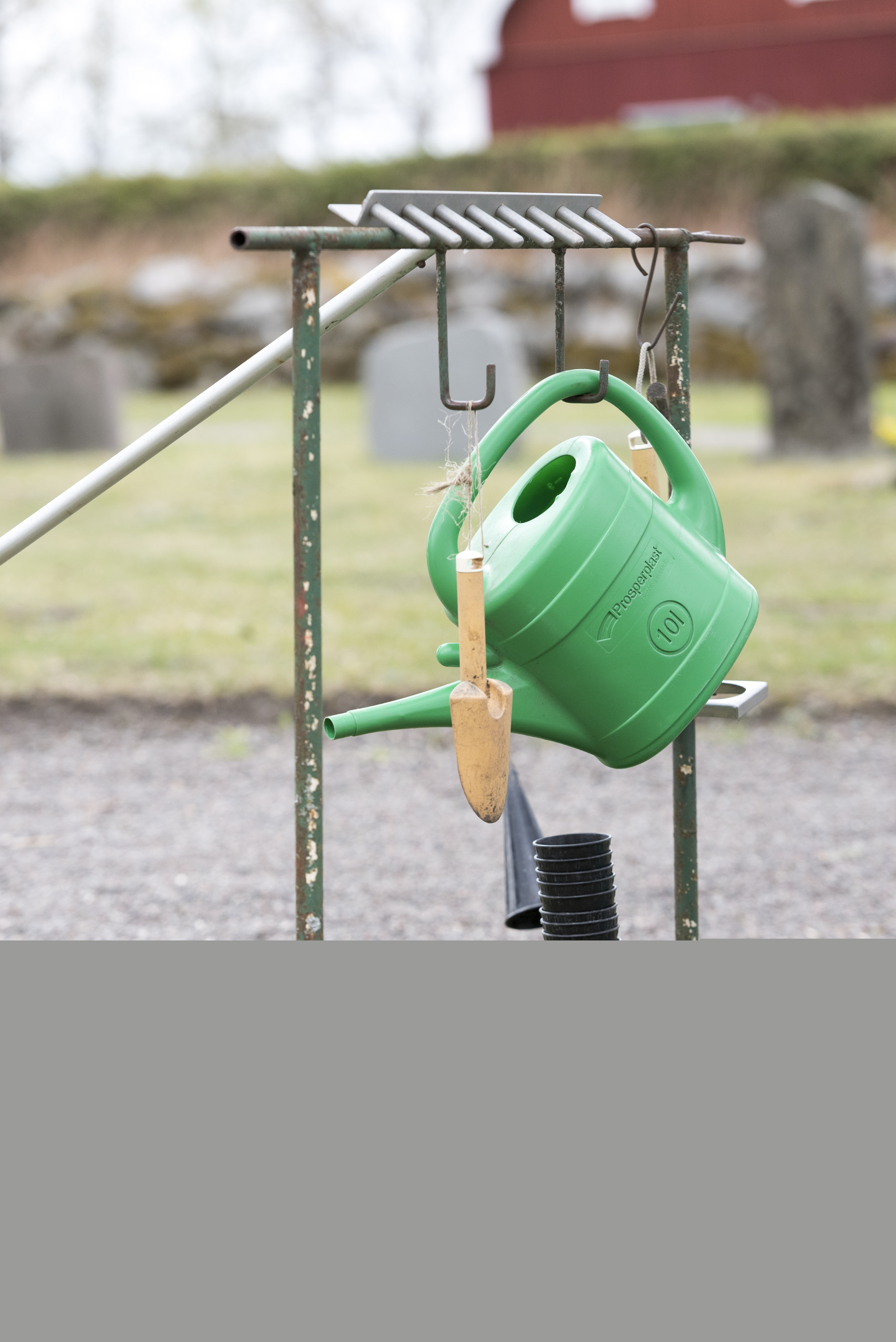 En vattenkanna och några verktyg hänger på en ställning vid en kyrkogård.