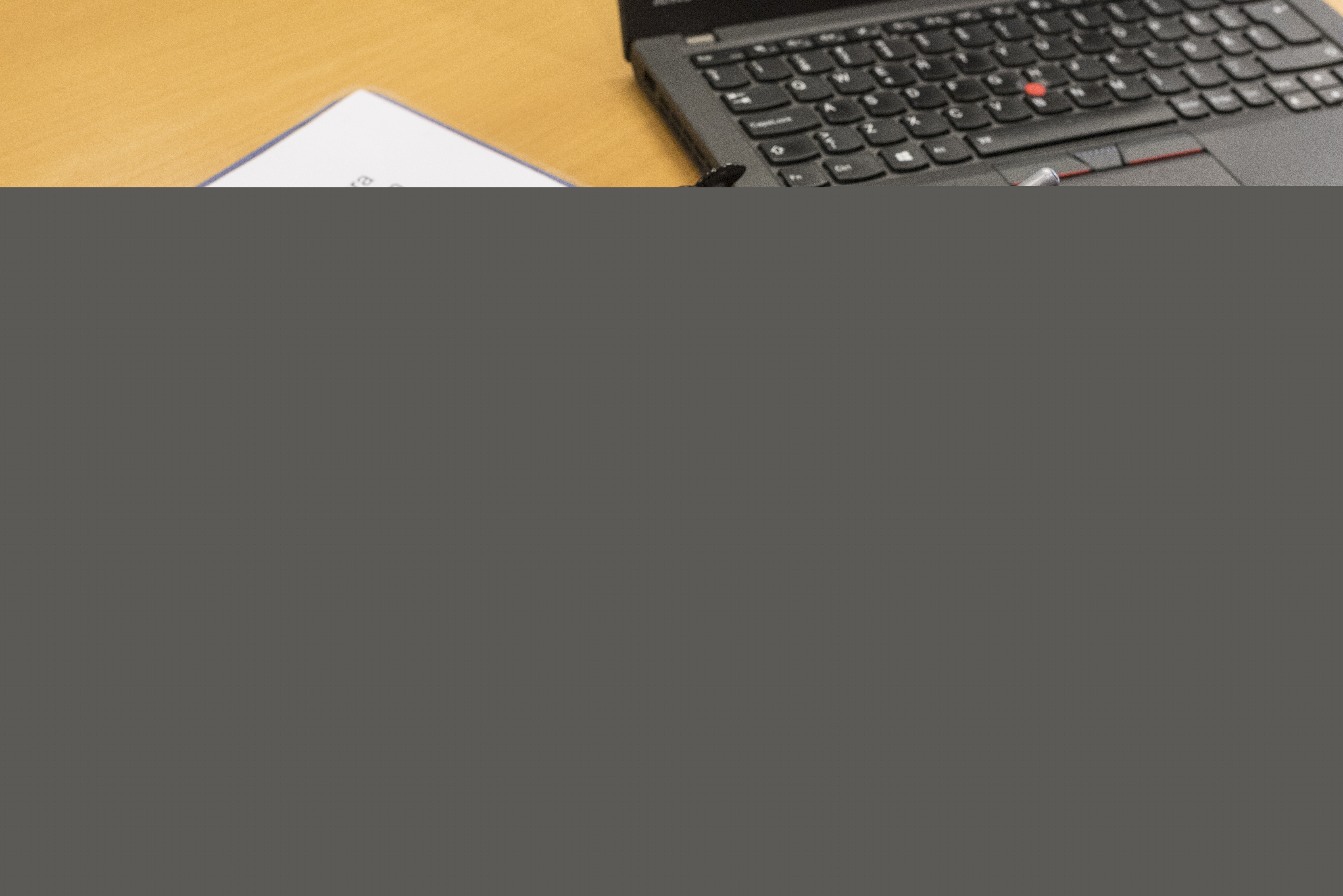 En person med en penna i handen sitter med ett texthäfte och en dator framför sig.