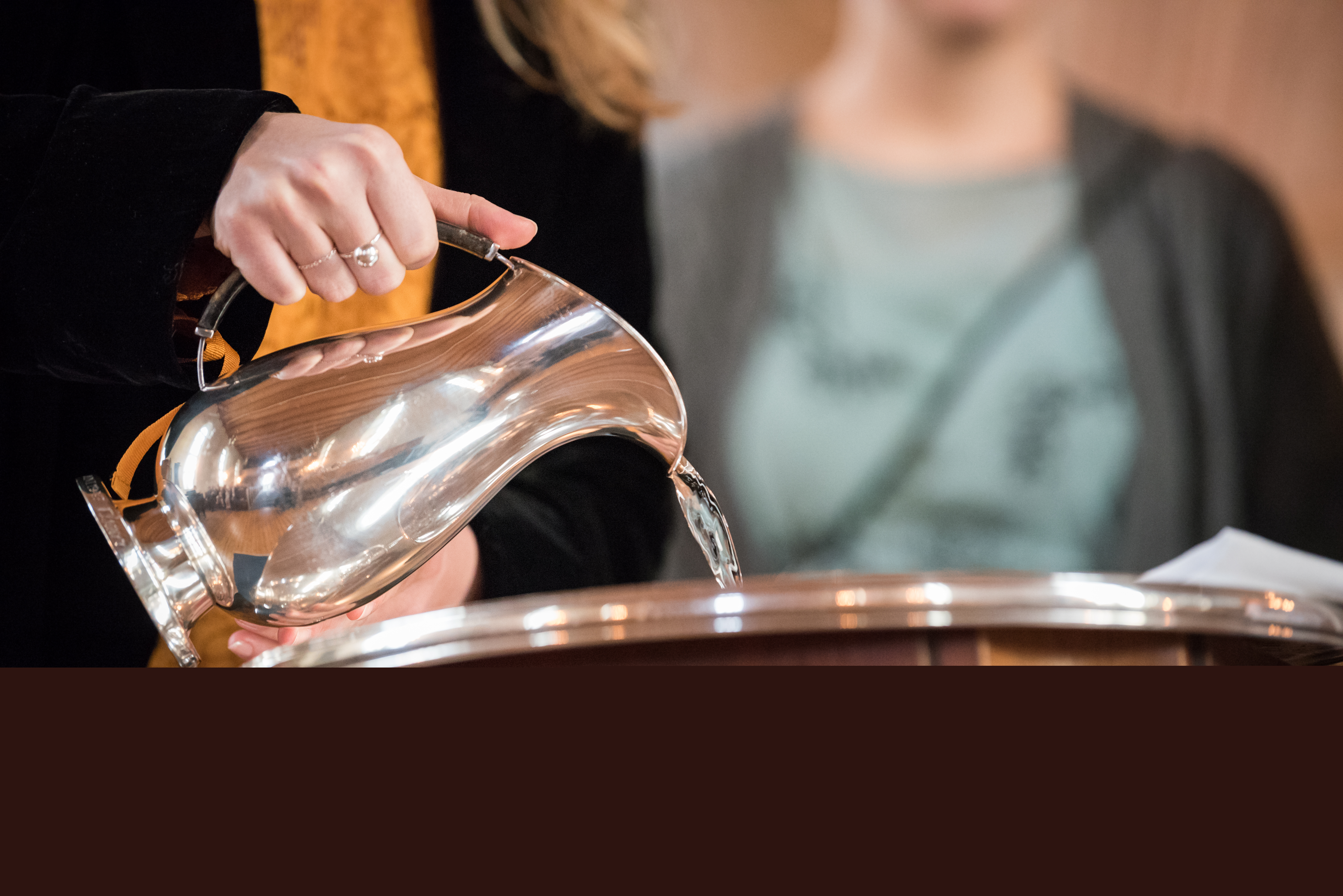 En kvinna häller vatten i en dopfunt från en silvrig kanna.