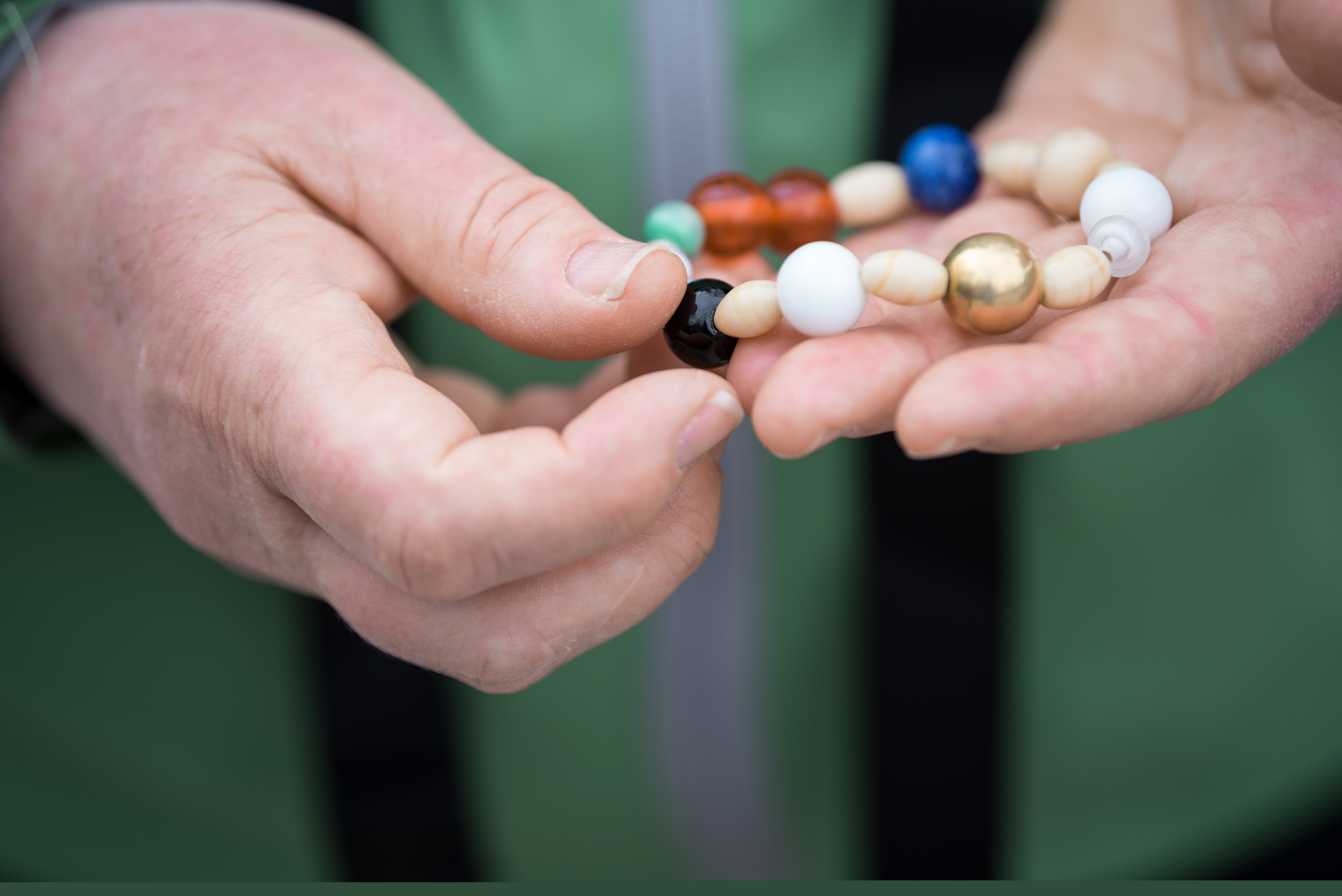 Närbild på någon som håller i ett pärlarmband  med pärlor i olika färger och former.