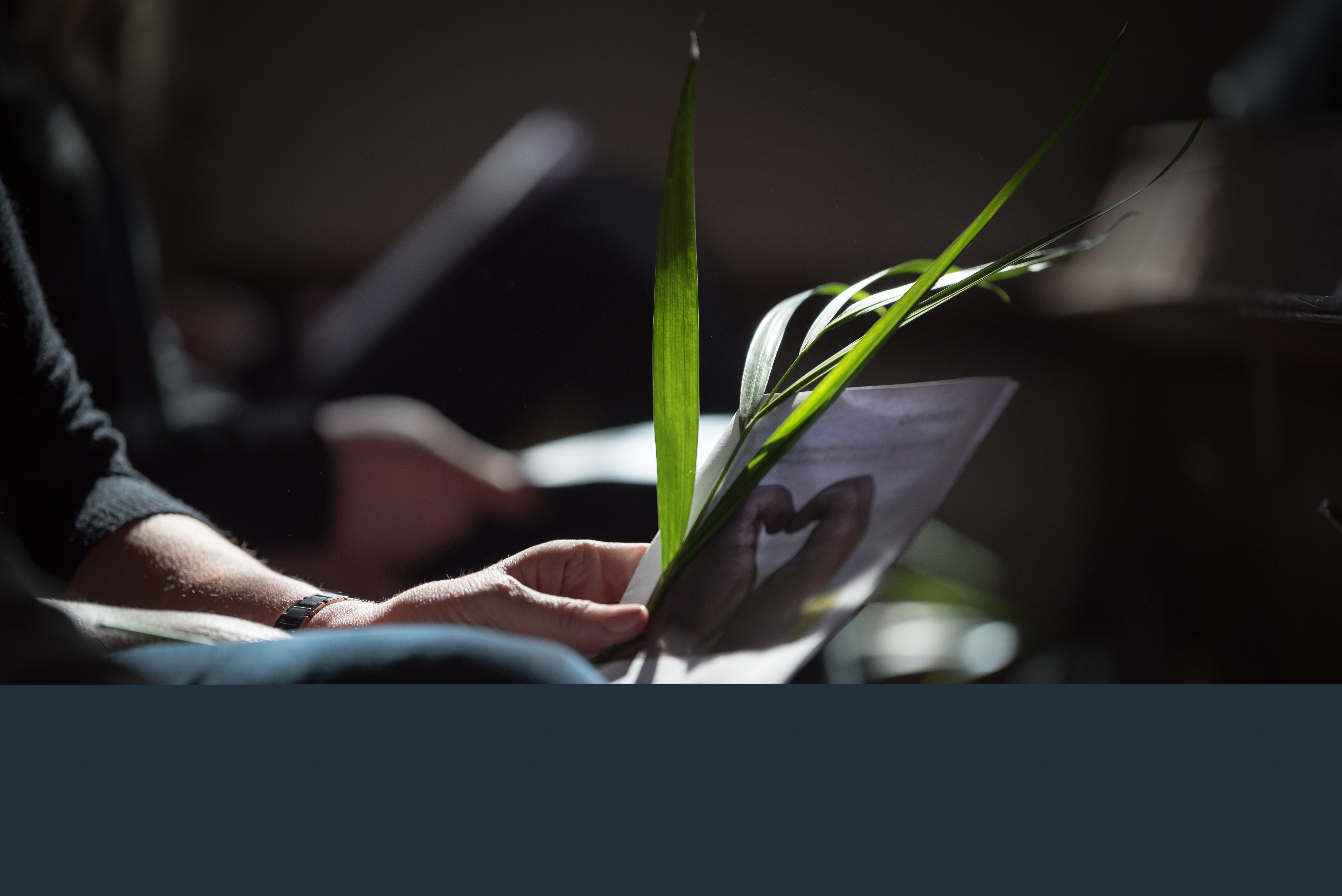 En person sitter med ett palmblad och ett häfte i händerna.