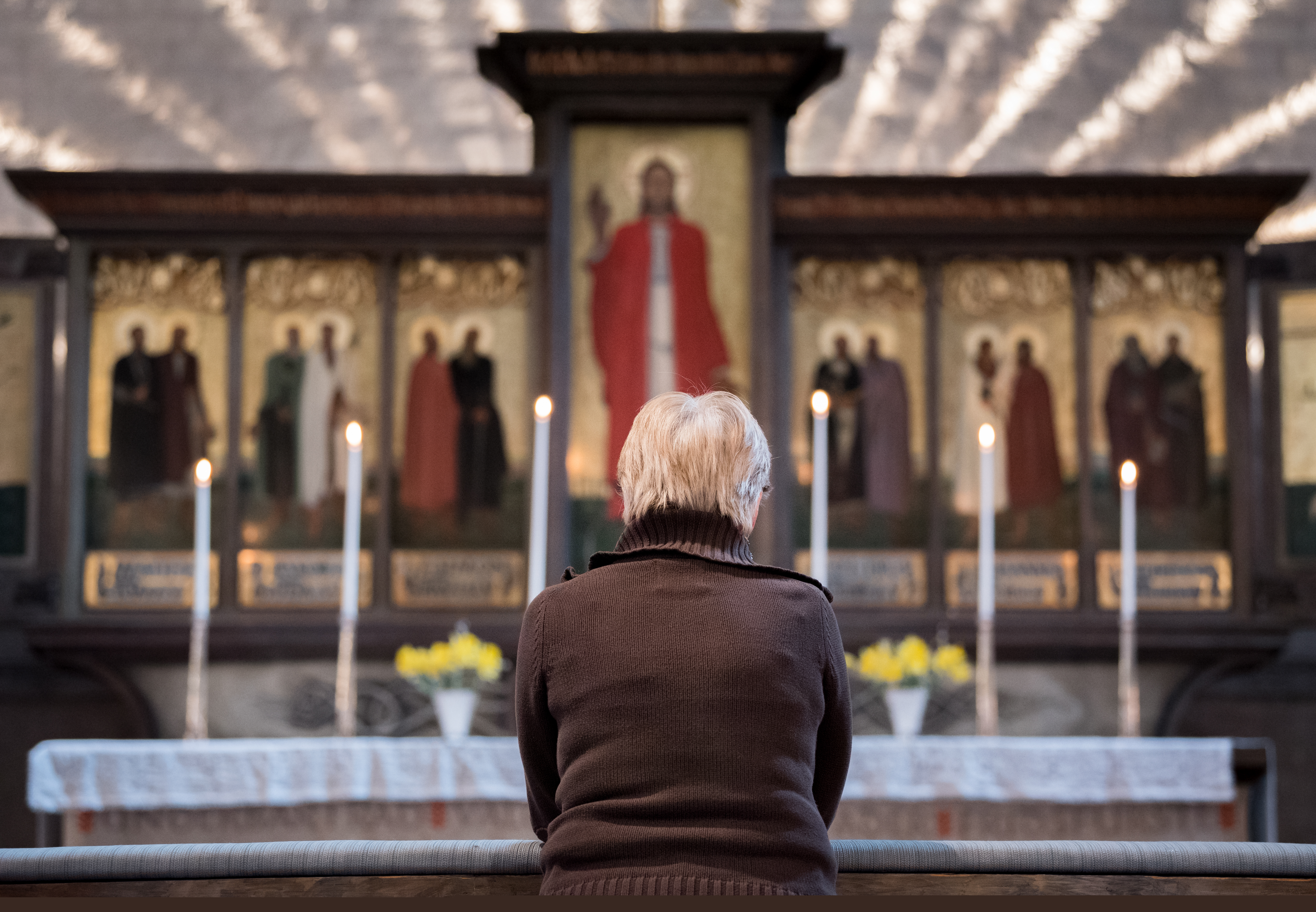 En kvinna sitter framför ett altare med en stor altartavla.