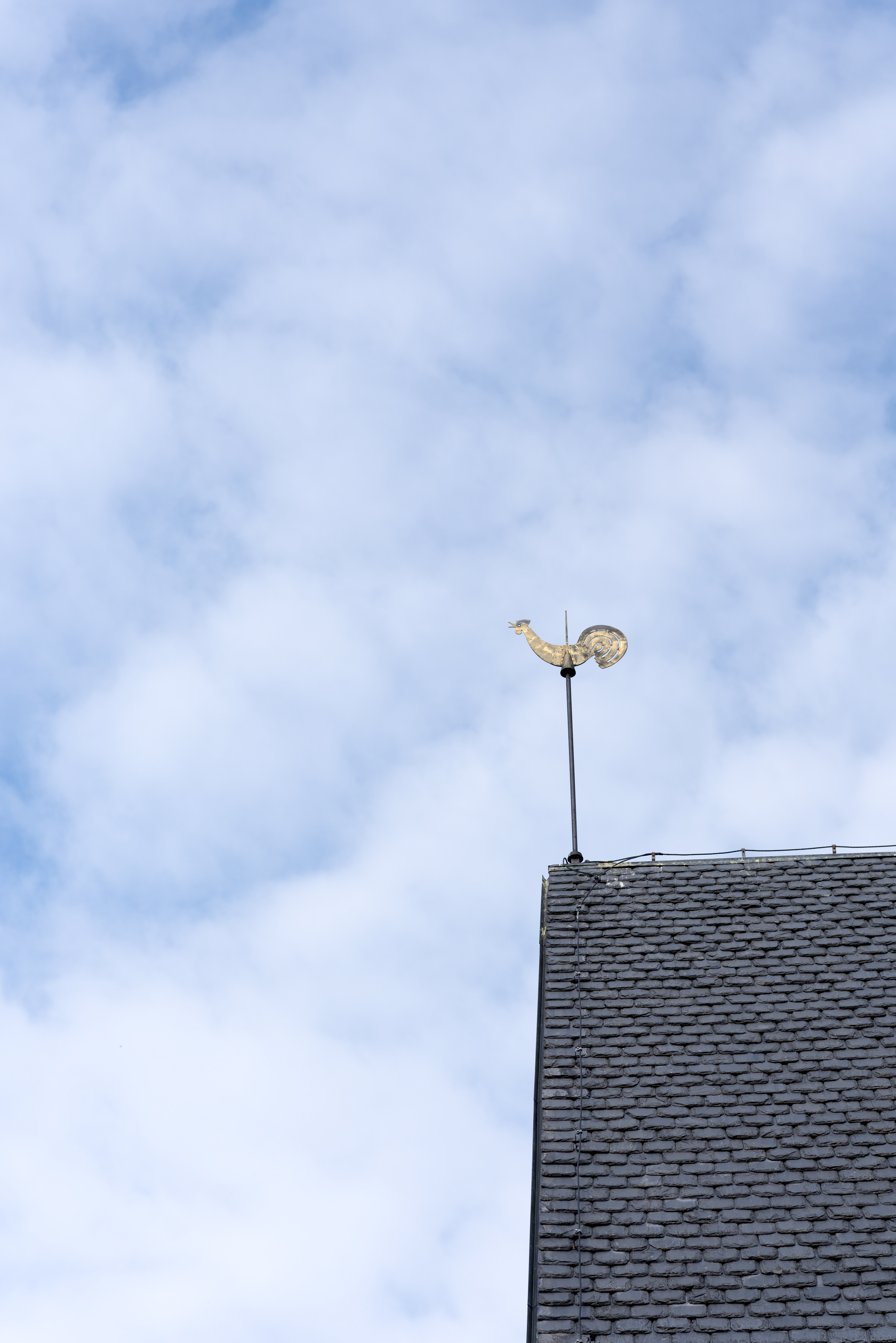 En kyrktupp på ett tak mot lätt molnig himmel.