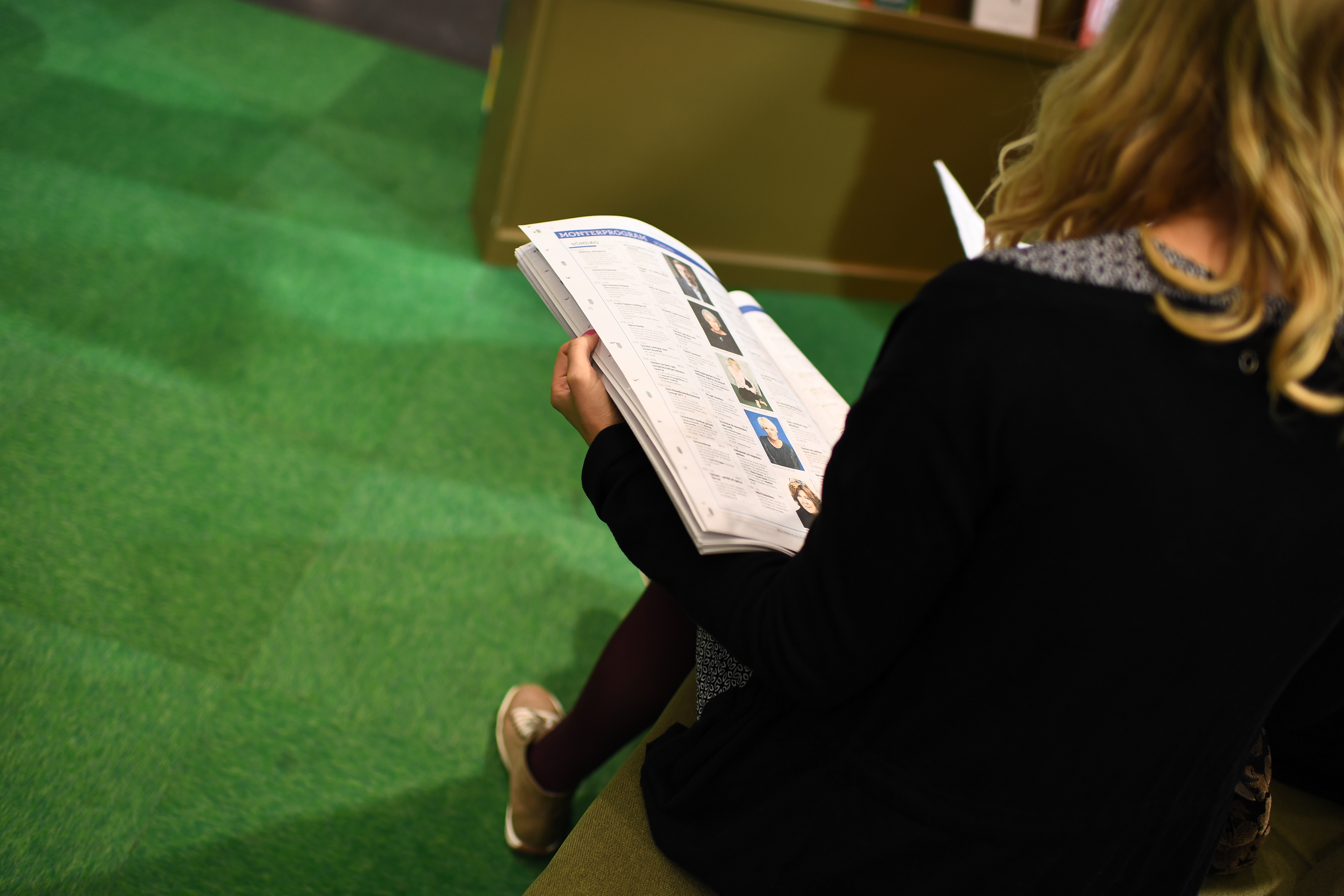 En kvinna sitter i en monter och bläddrar i en tidning.