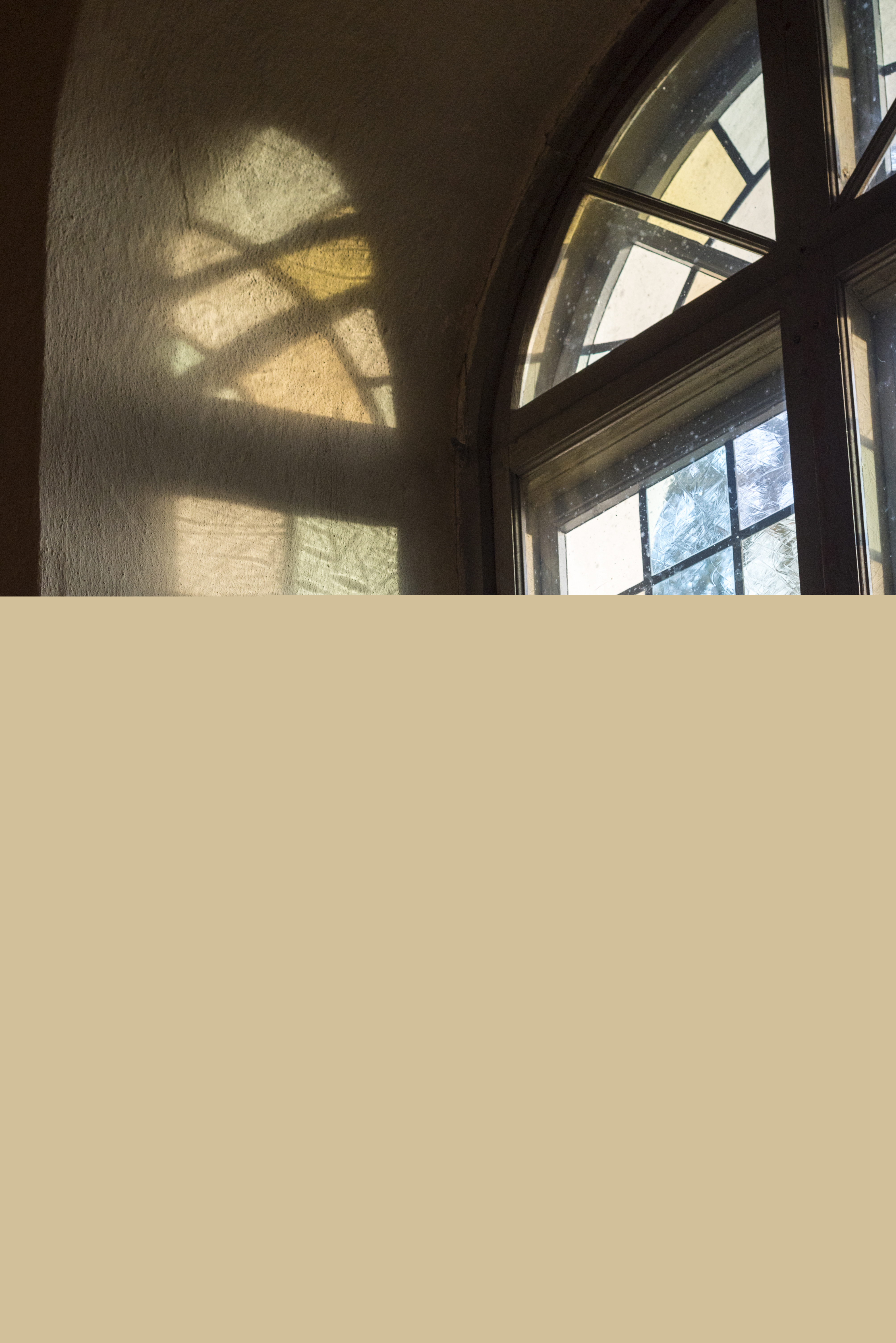 Solen reflekteras på en vit vägg genom ett färgat kyrkfönster.