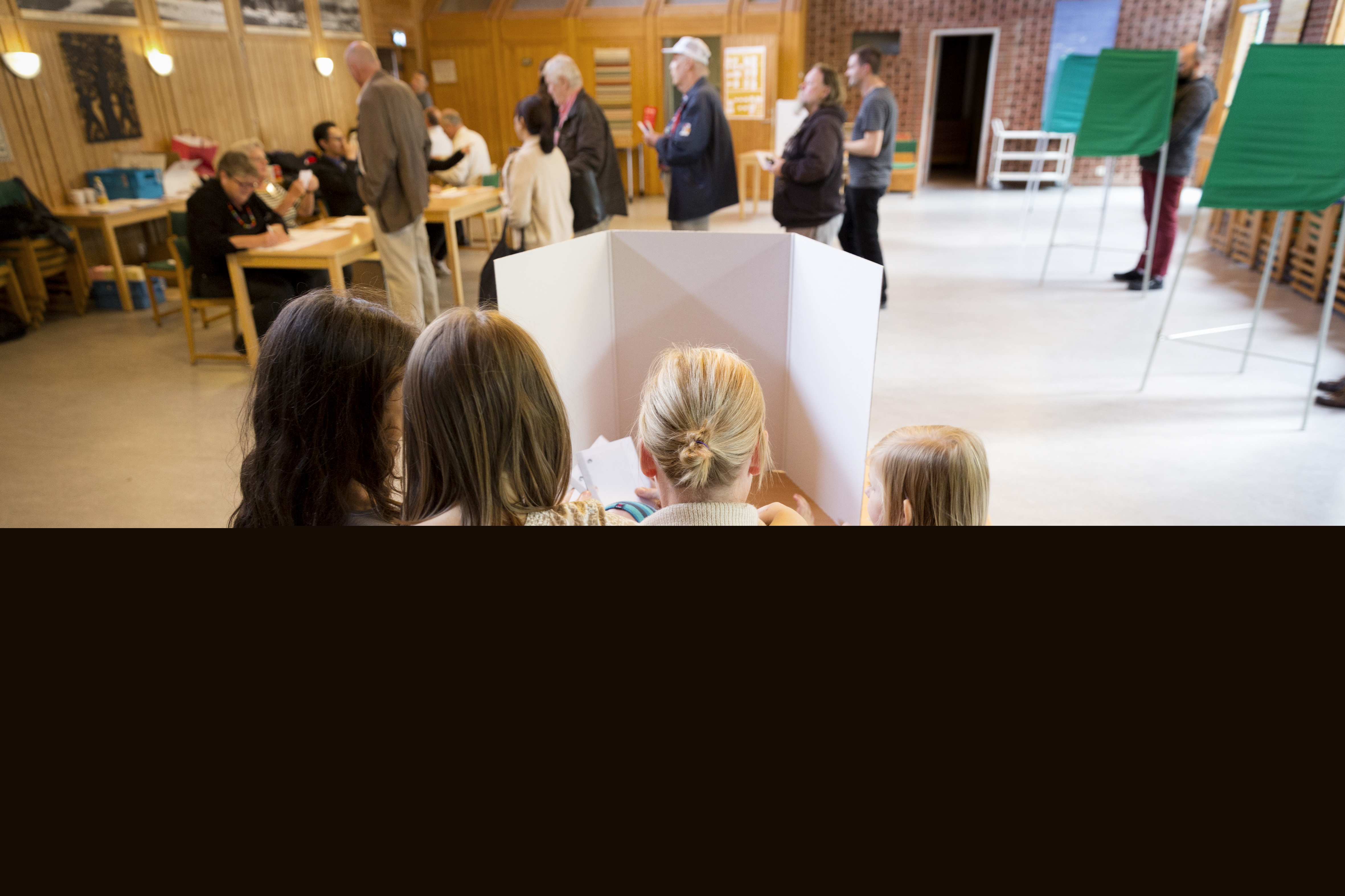 Tre små flickor står runt sin mamma i ett röstbås.