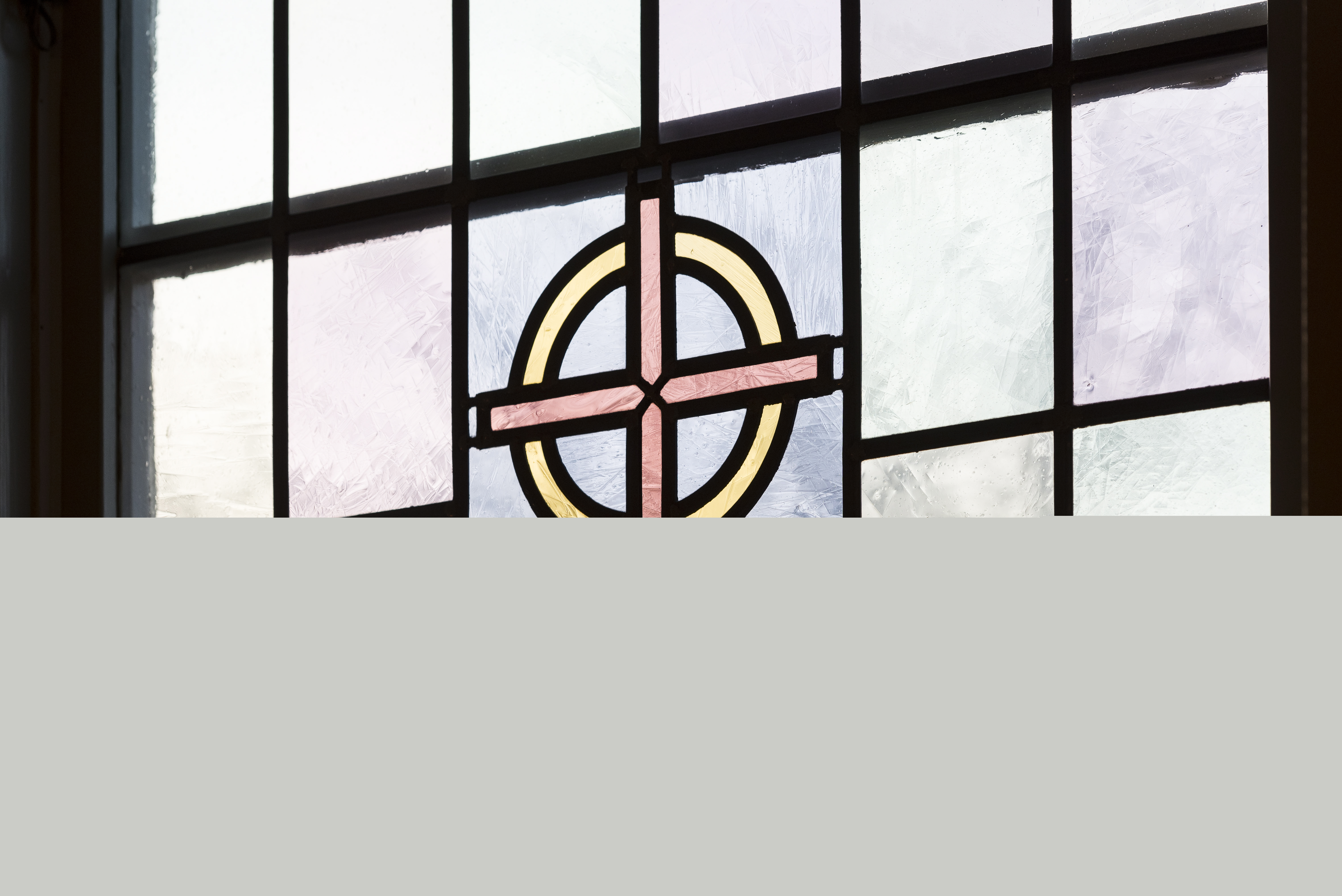 Närbild på ett färgat kyrkfönster med ett kors i mitten.