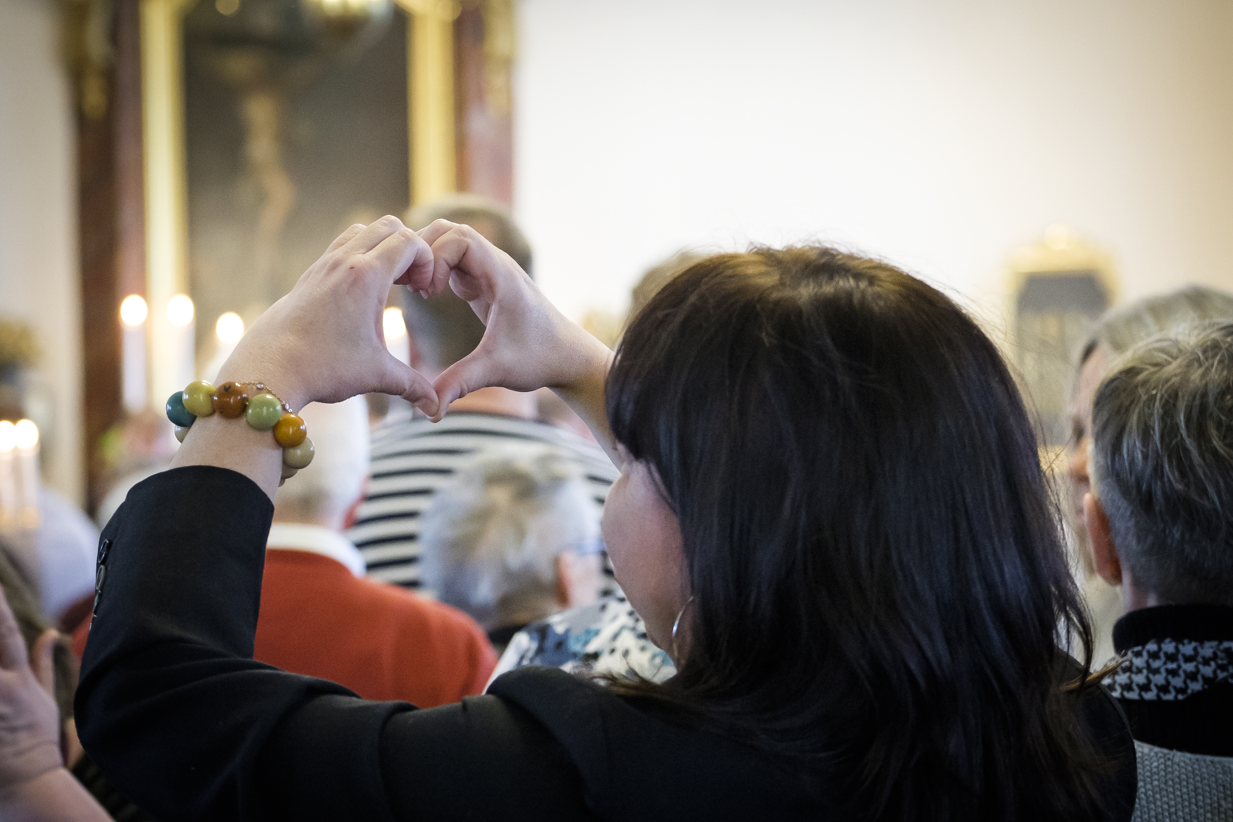 En kvinna står bland en massa människor och gör ett hjärta med händerna.