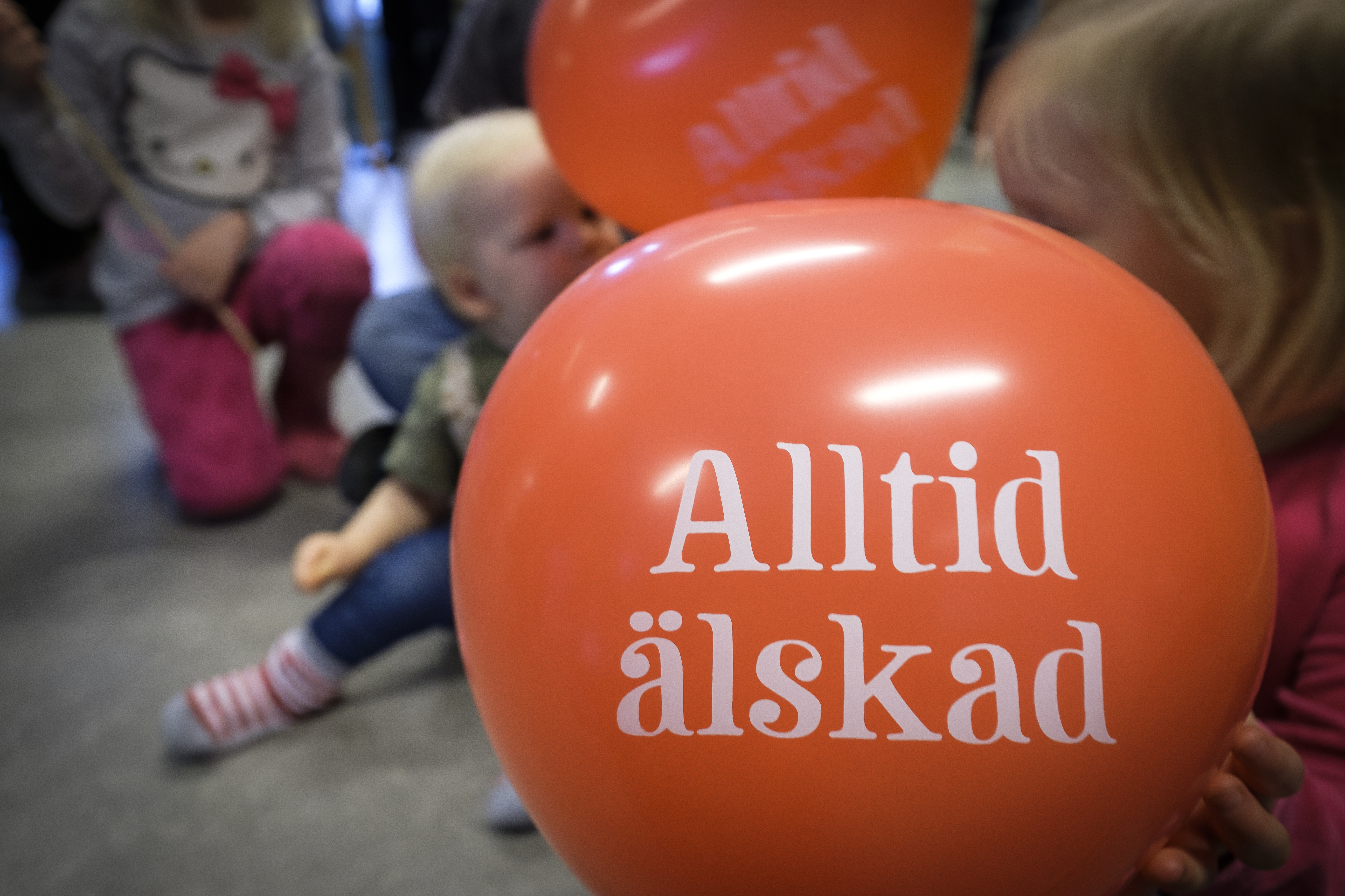 Några små barn med röda ballonger med texten Alltid älskad.