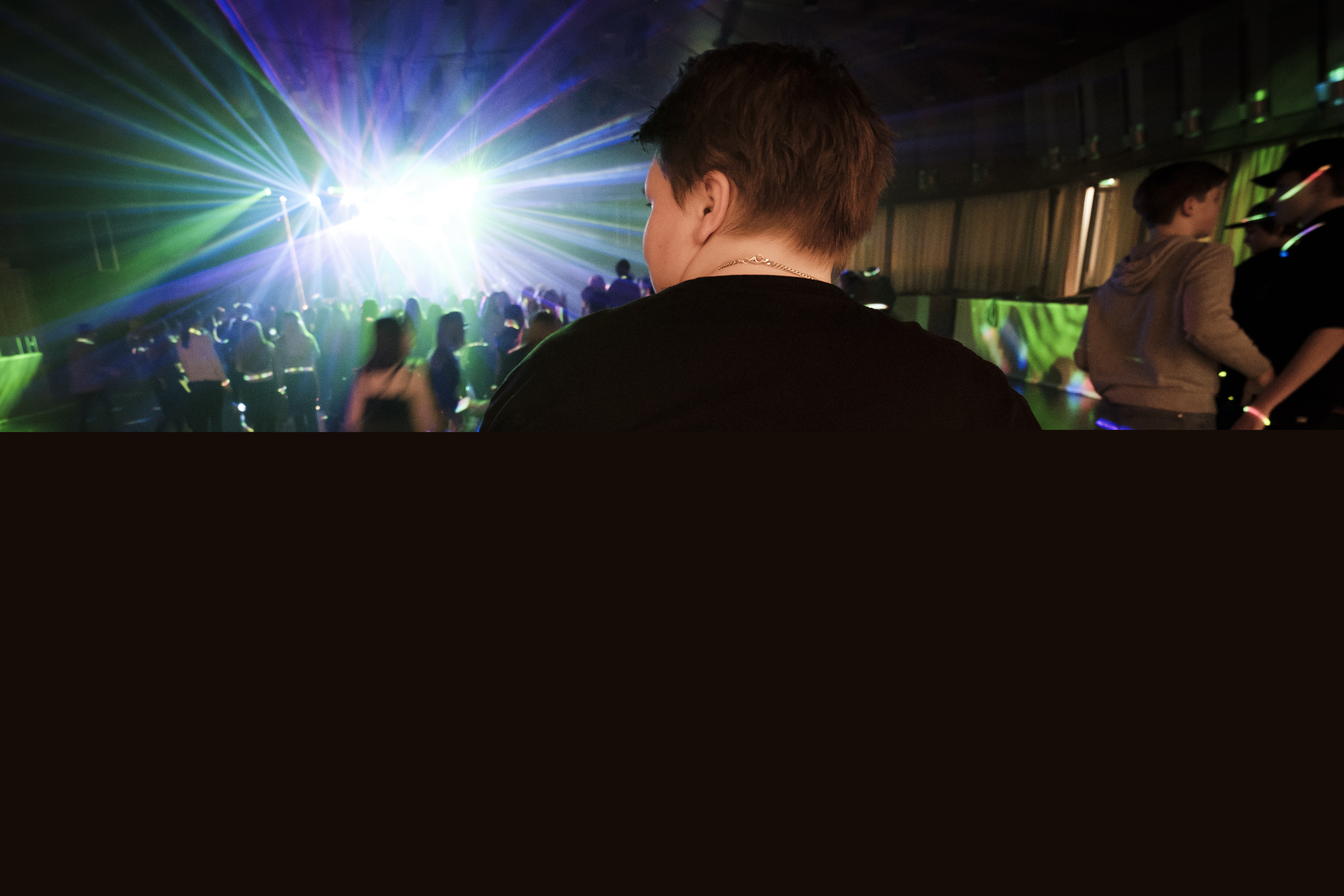 En ungdom har en tröja med texten Svenska kyrkans unga på ryggen. I bakgrunden syns ett fullt dansgolv med discoljus.