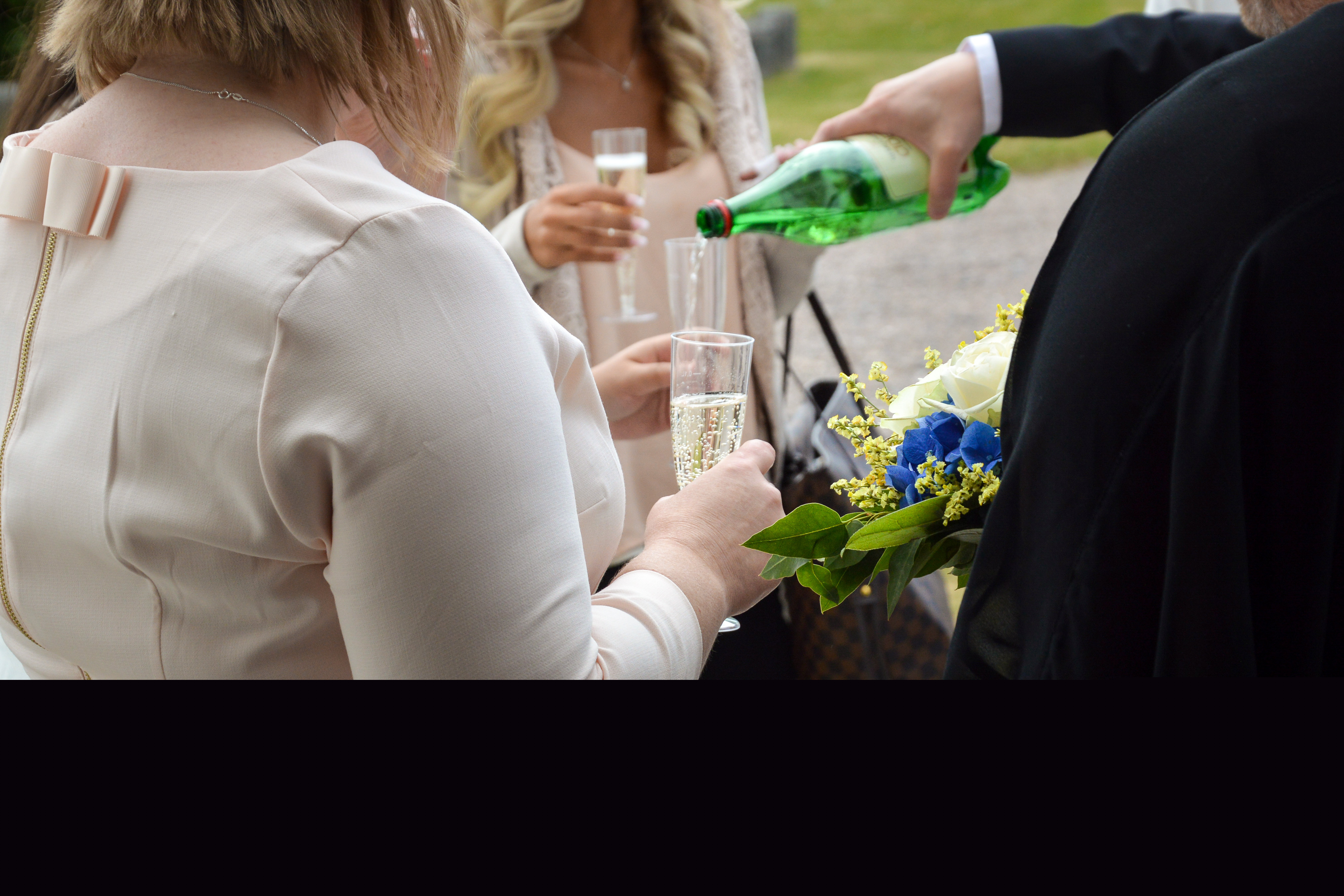 Någon i kostym står utomhus och häller upp cider till några kvinnor.