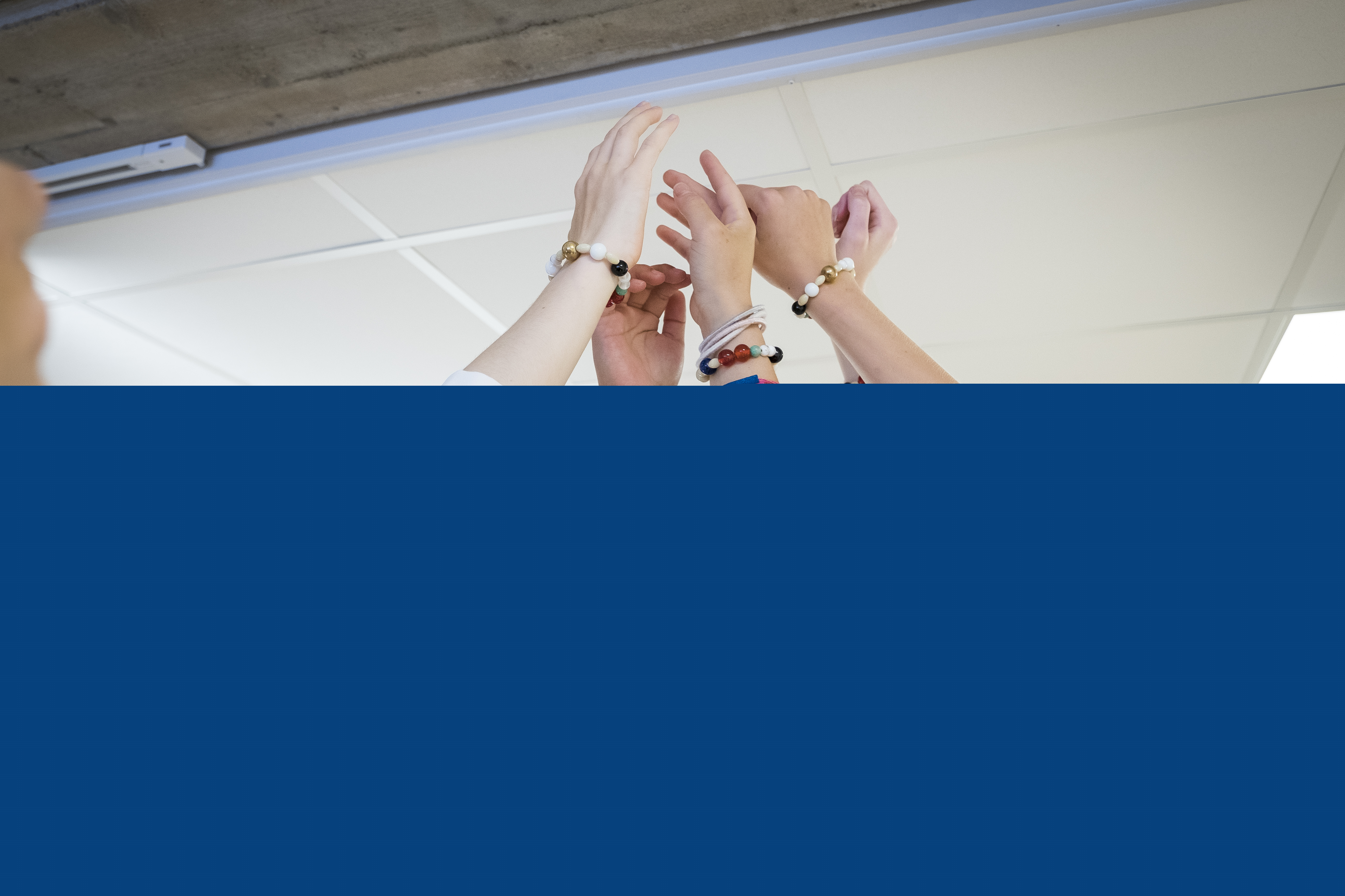 Några konfirmander står i ring och håller upp händerna mot taket.