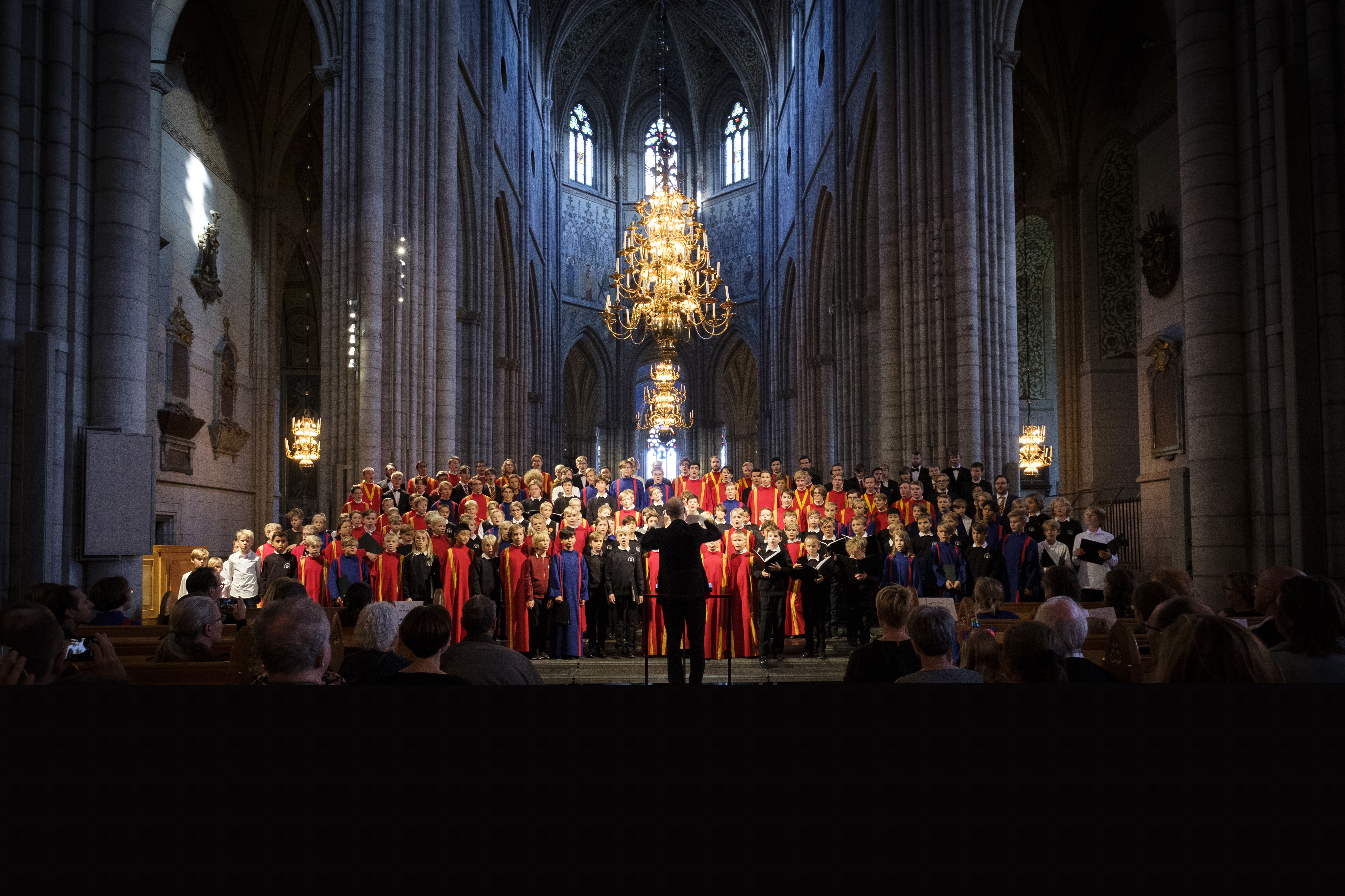 Uppsala domkyrkas gosskör i rödgula och blåa kåpor sjunger i en fullsatt domkyrka.