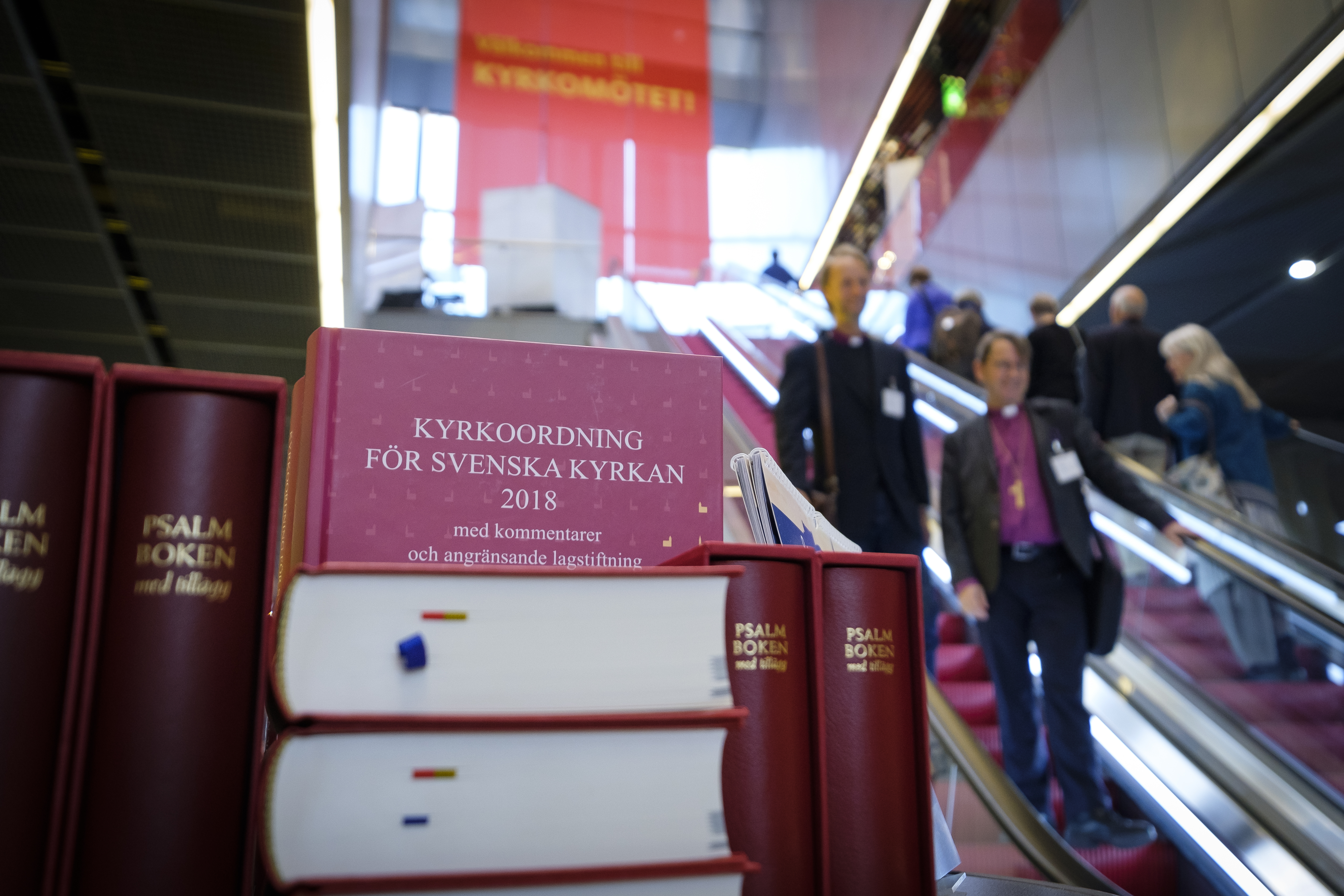 Vid en röd rulltrappa ligger en hög med psalmböcker och boken Kyrkoordning för Svenska kyrkan.