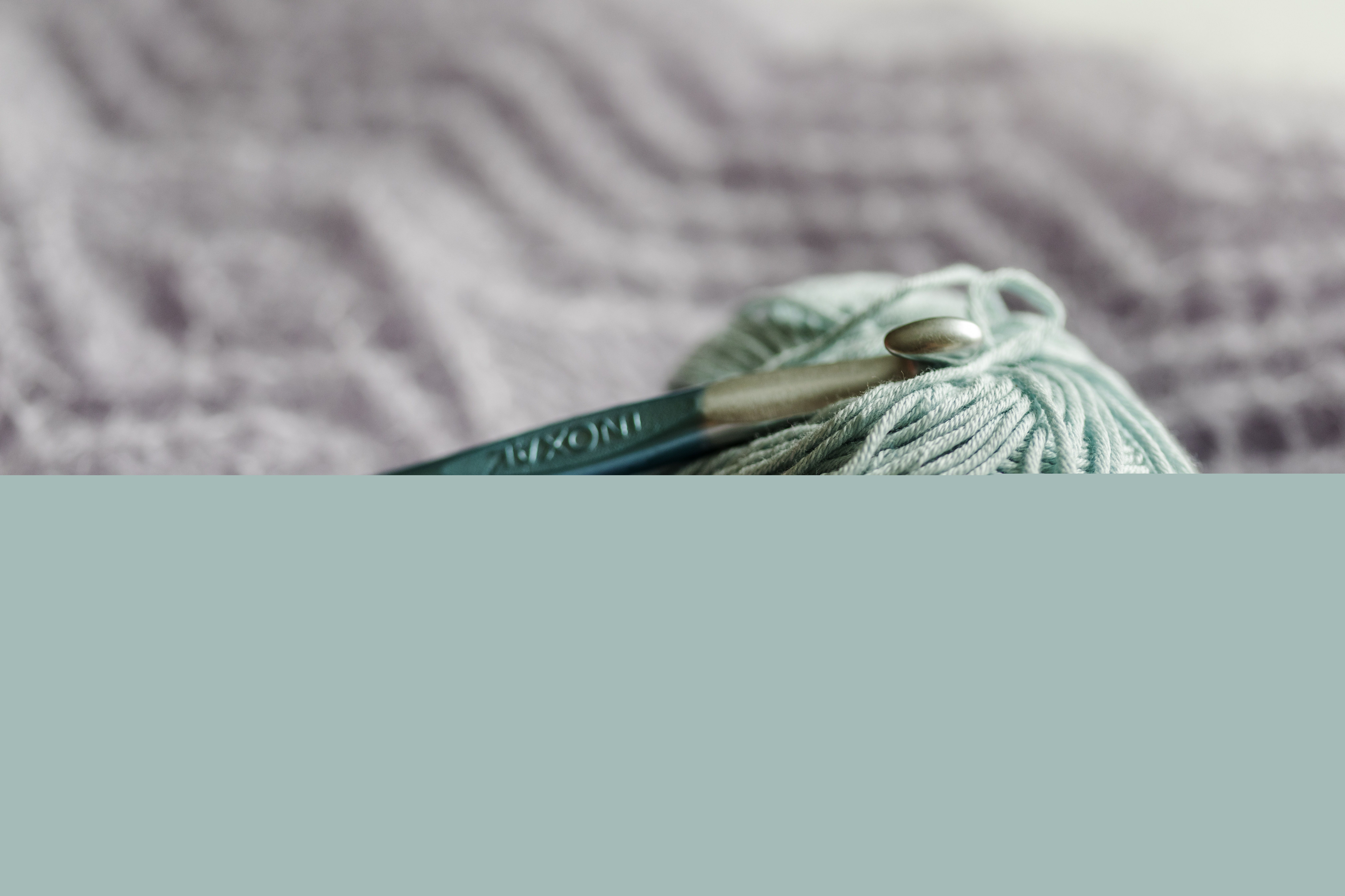 Ett turkost garnnystan och två stickor ligger på en filt.