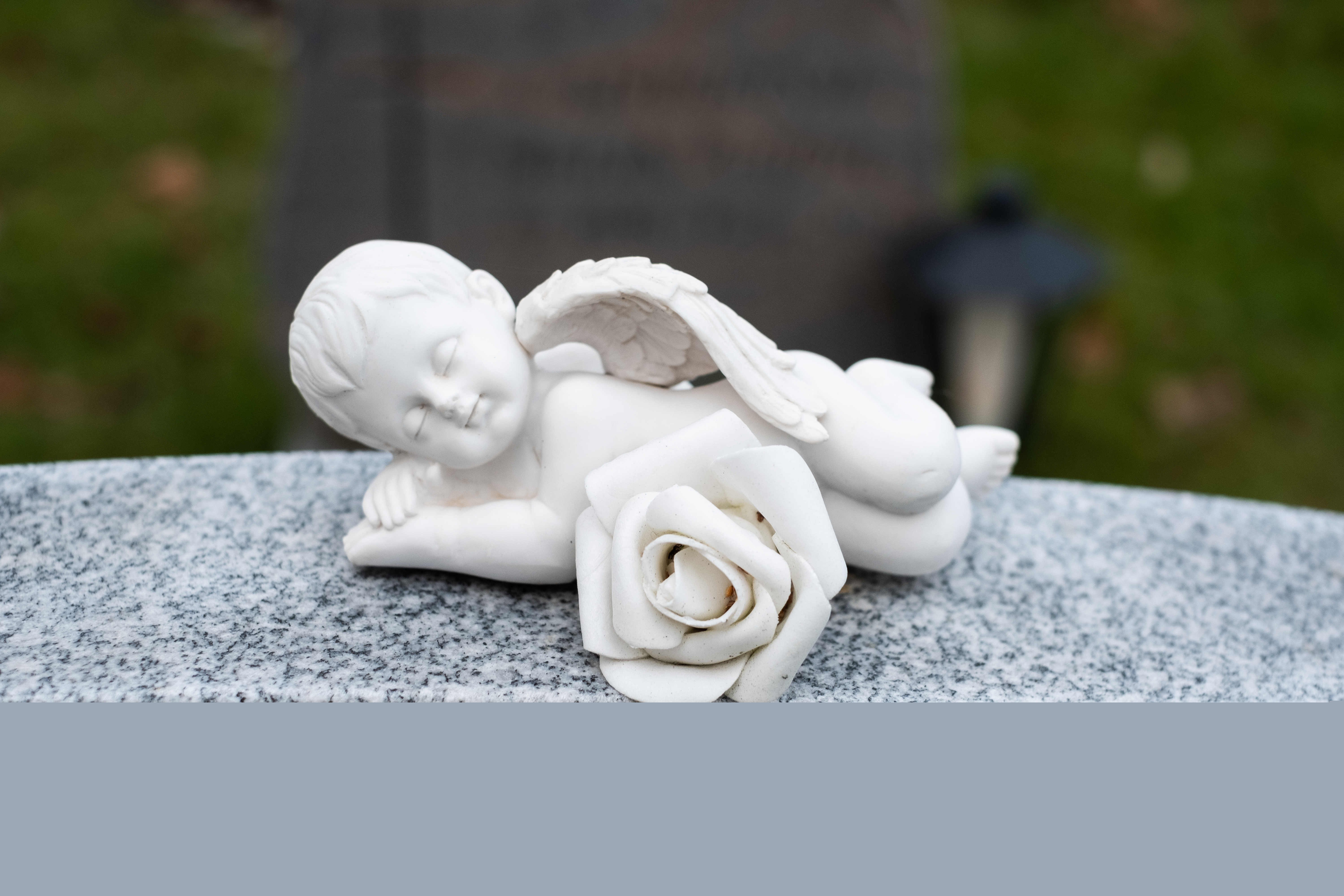 En liten sovande ängel i porslin ligger på en gravsten.