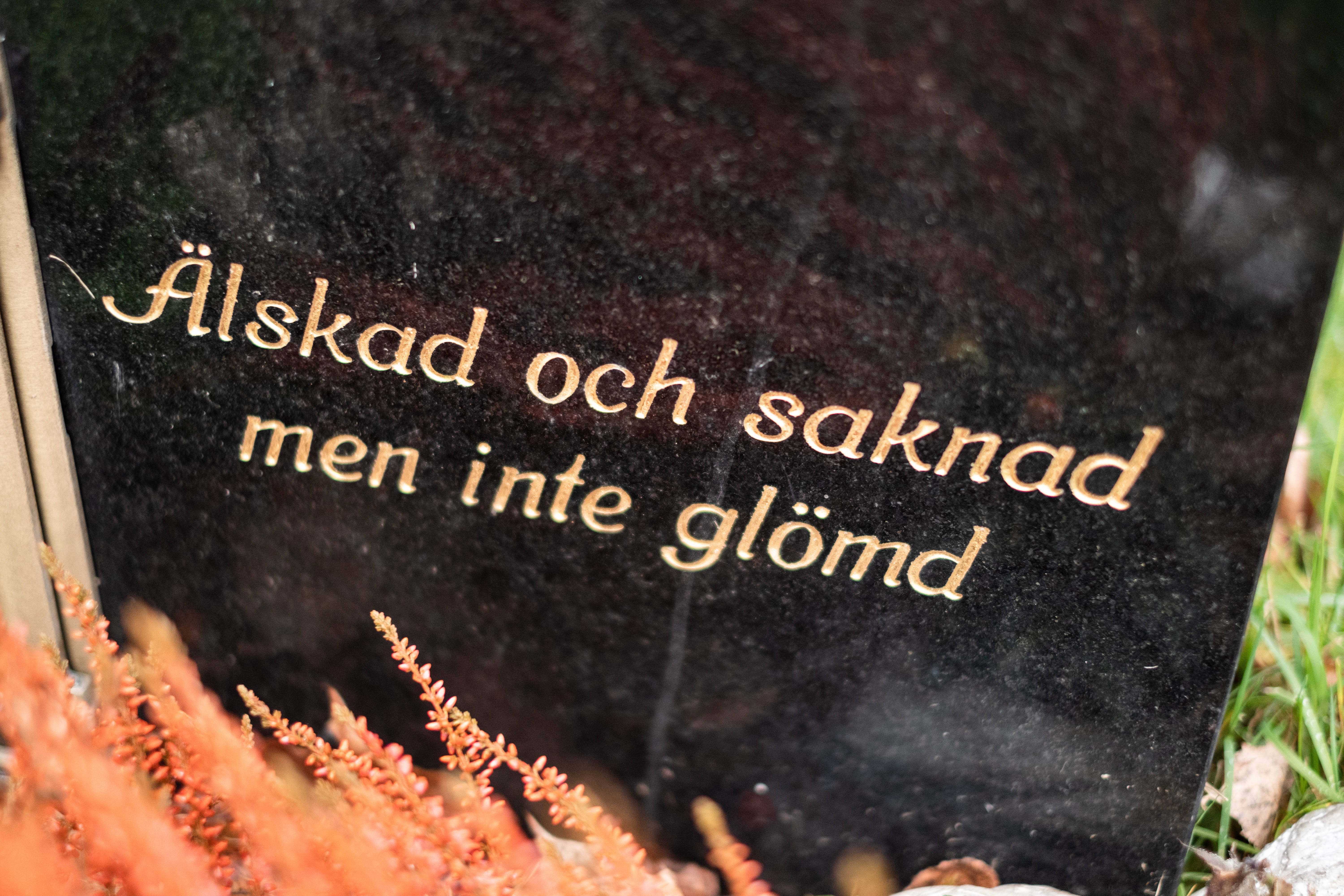 En svart gravsten med guldfärgad text: Älskad och saknad men inte glömd.