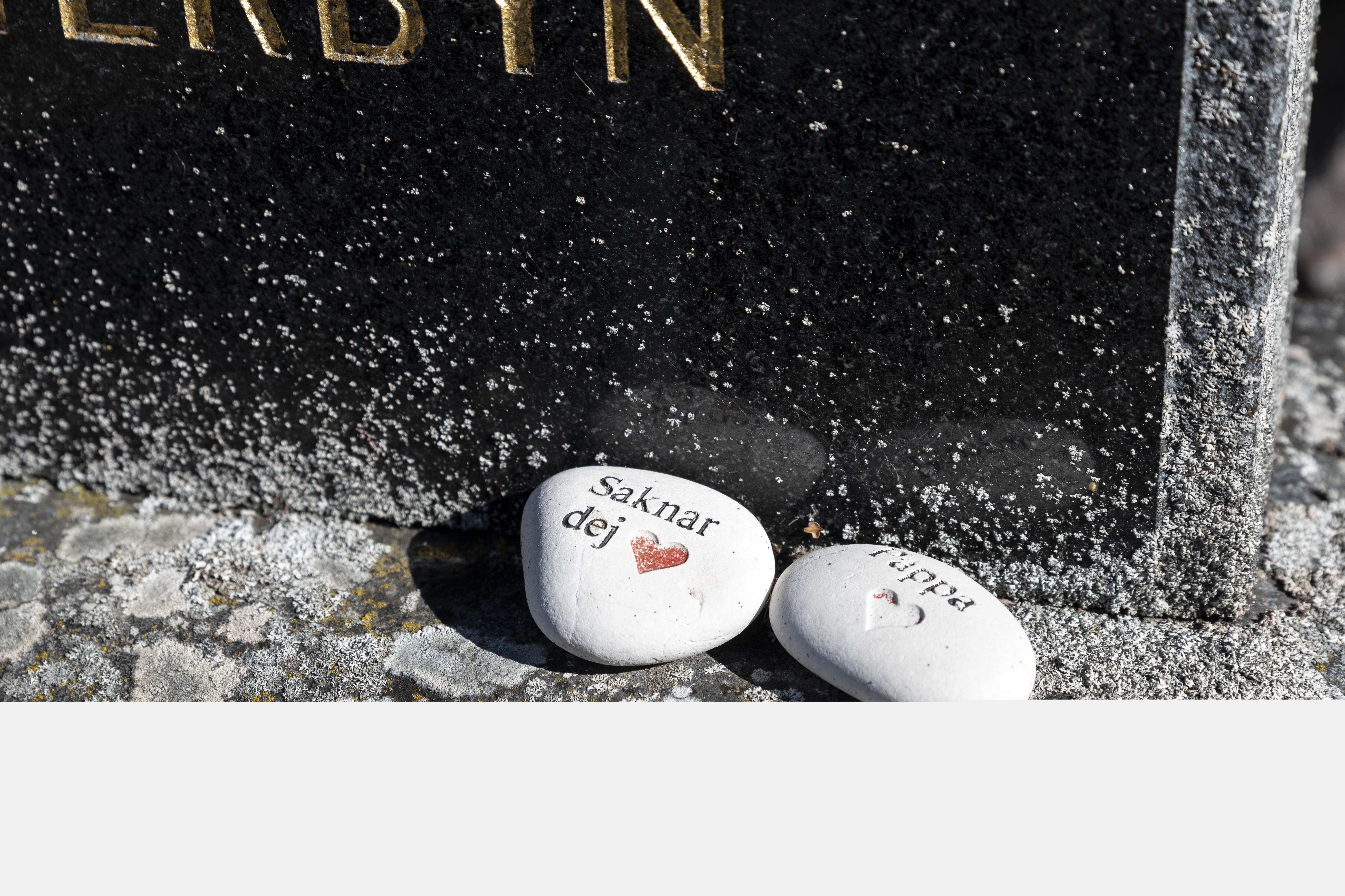 Två vita stenar med texterna Saknar dej och Pappa ligger på en gravsten.