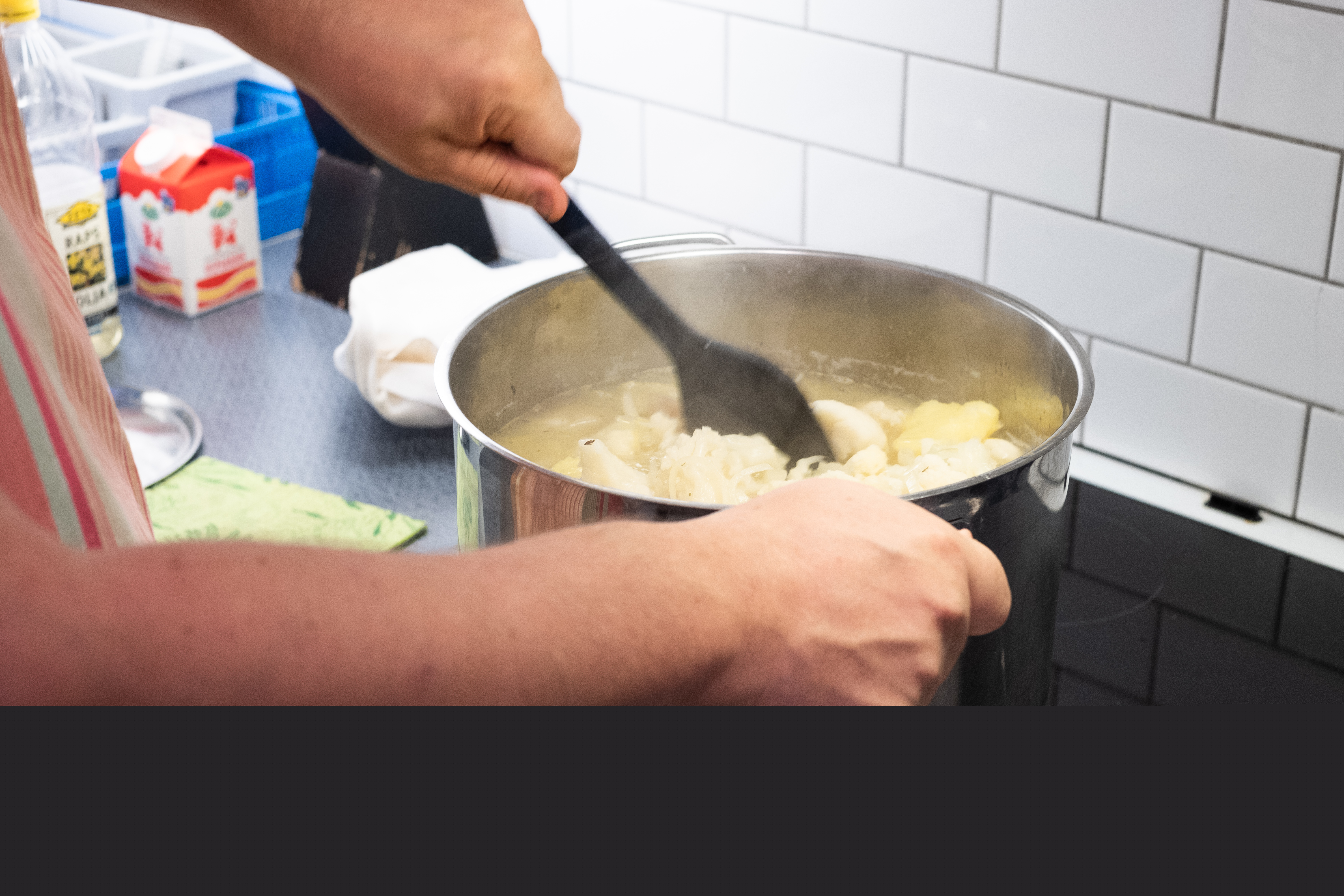 Någon rör om i en stor kastrull på spisen.