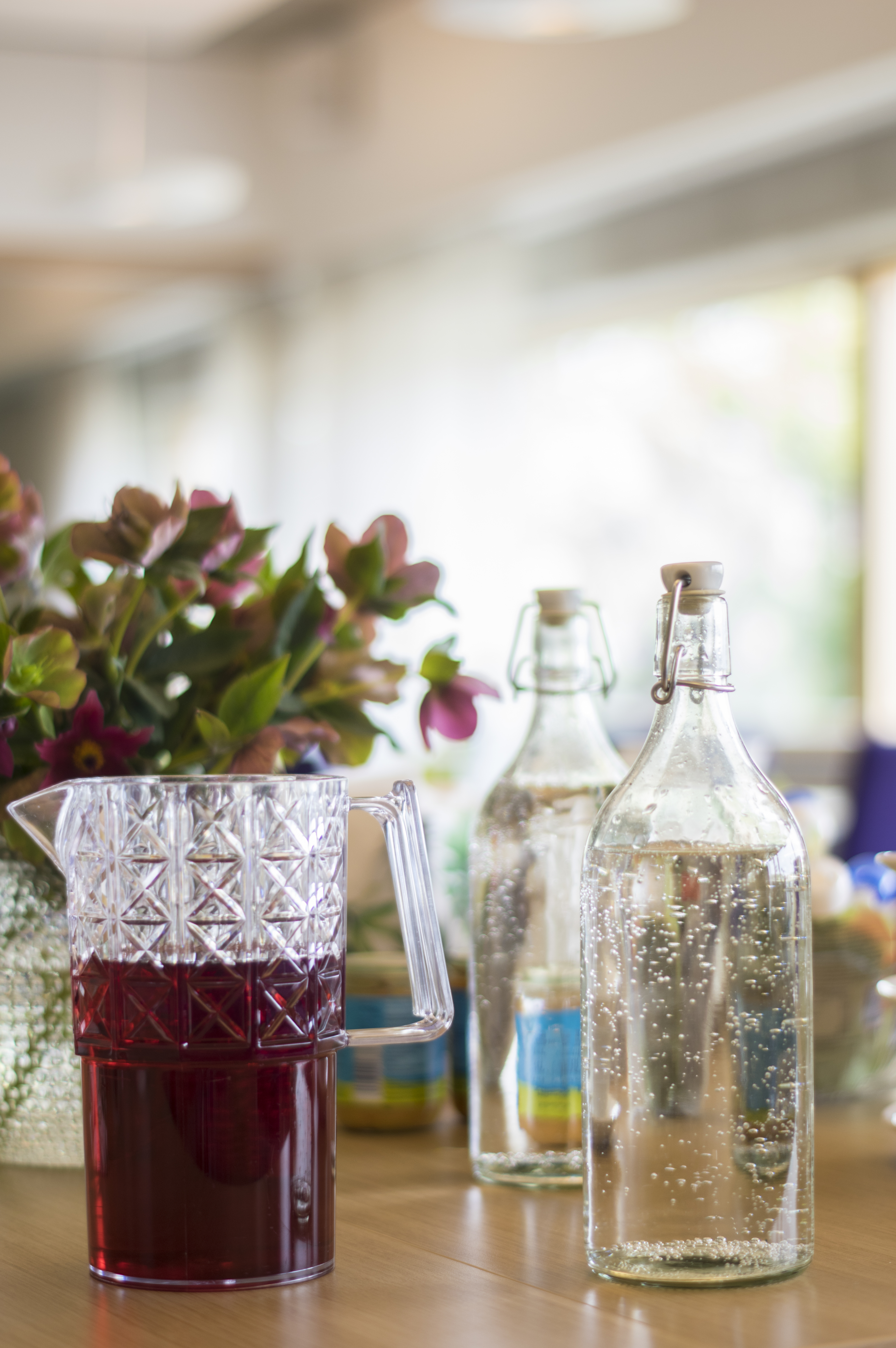 En karaff med saft och några glasflaskor vatten står på ett bord.