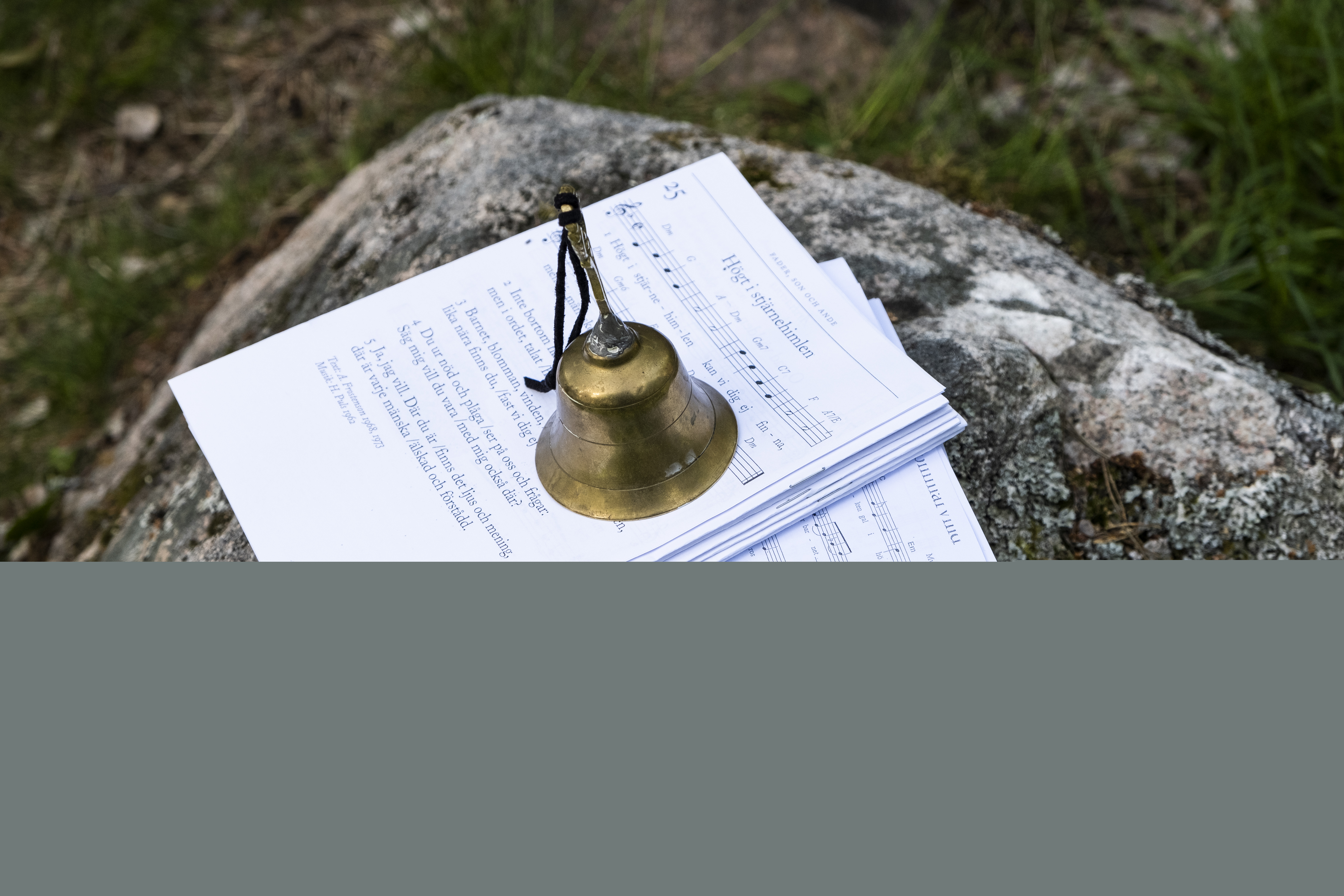 På en sten ligger notpapper. En ringklocka står ovanpå så de inte blåser iväg.