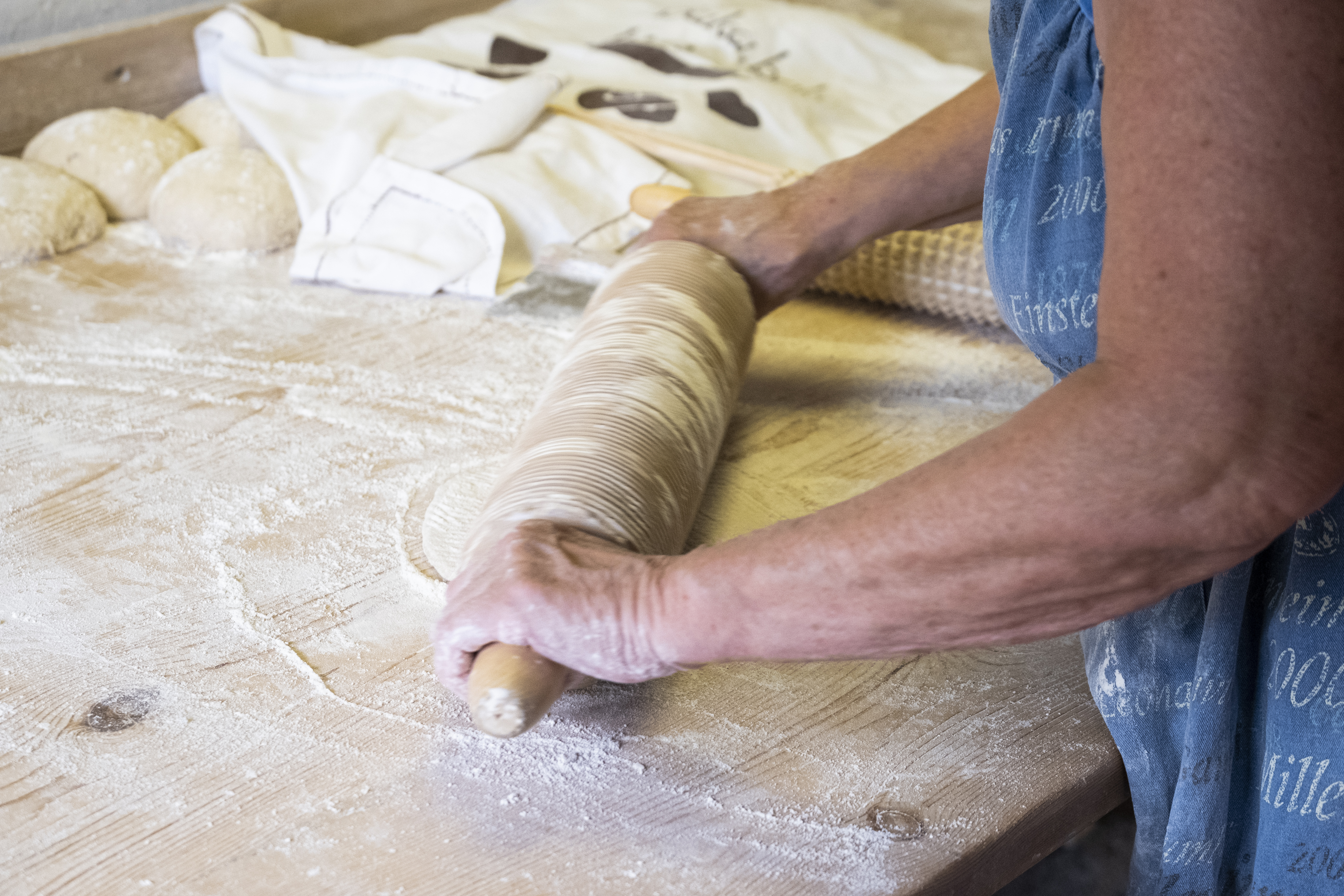 Någon kavlar ut en deg på en mjölad bänk.