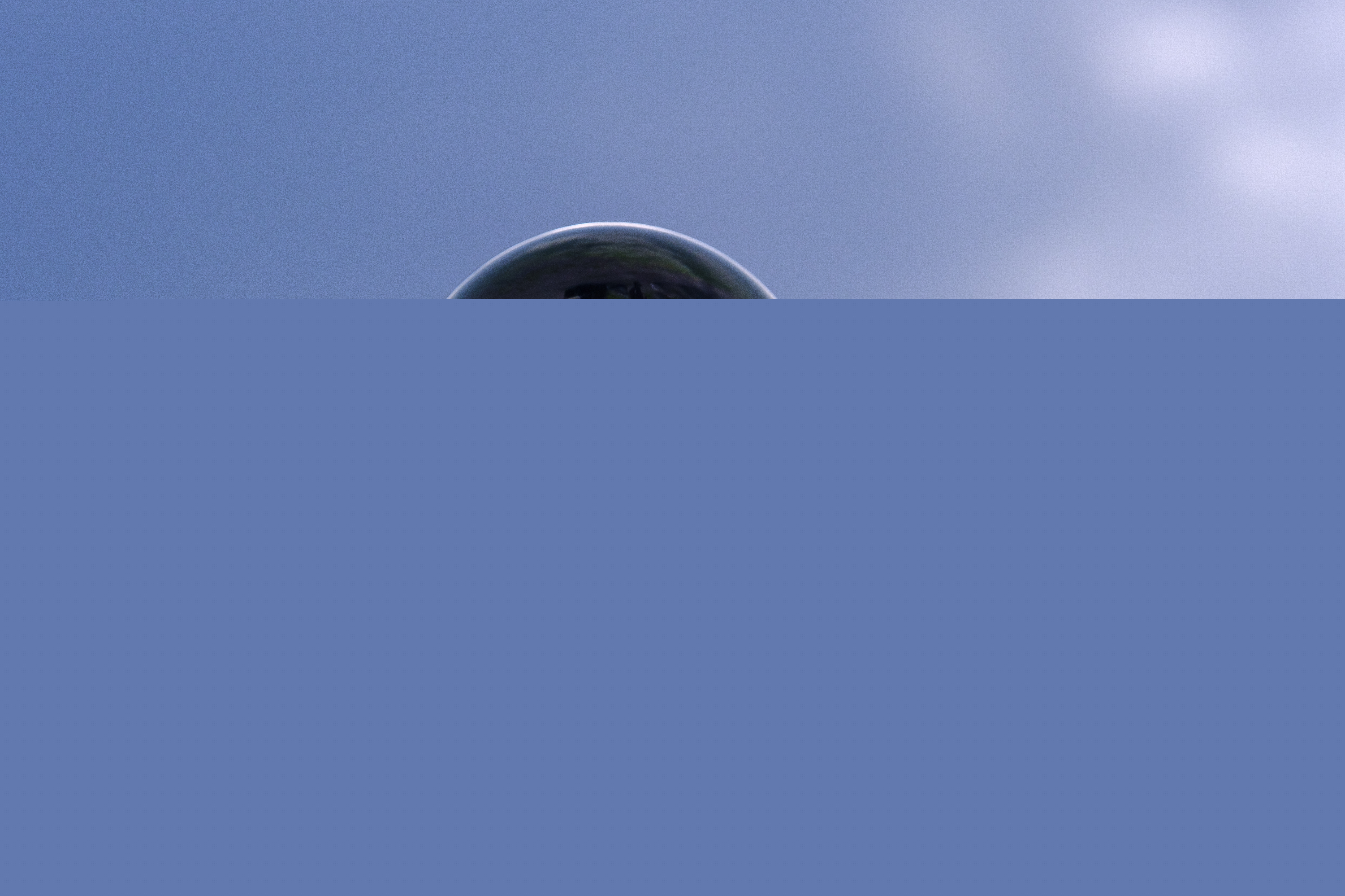 En kupad hand håller ett glasklot. Blå himmel i bakgrunden.